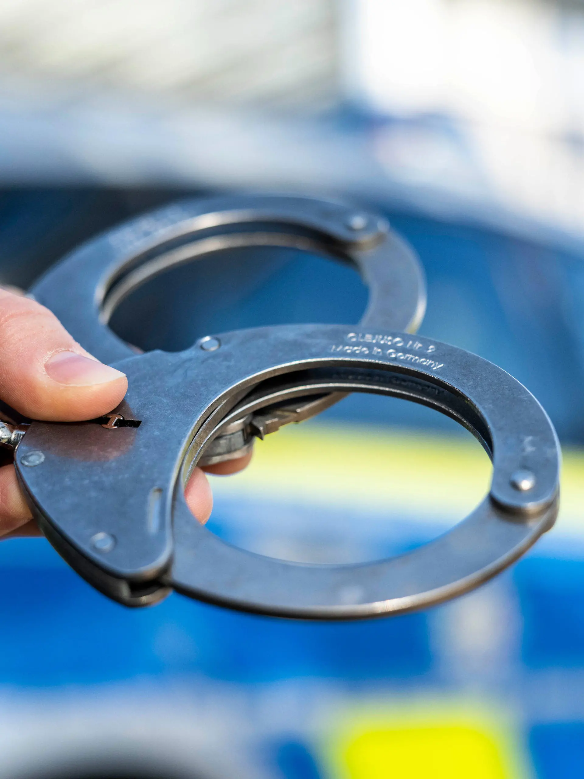 ARCHIV - 28.09.2021, Nordrhein-Westfalen, Gütersloh: Eine Hand hält Handschellen vor einen Streifenwagen der Polizei. Am 05.04.2022 wird in Berlin die Polizeiliche Kriminalstatistik 2021 vorgestellt. Foto: David Inderlied/dpa +++ dpa-Bildfunk +++