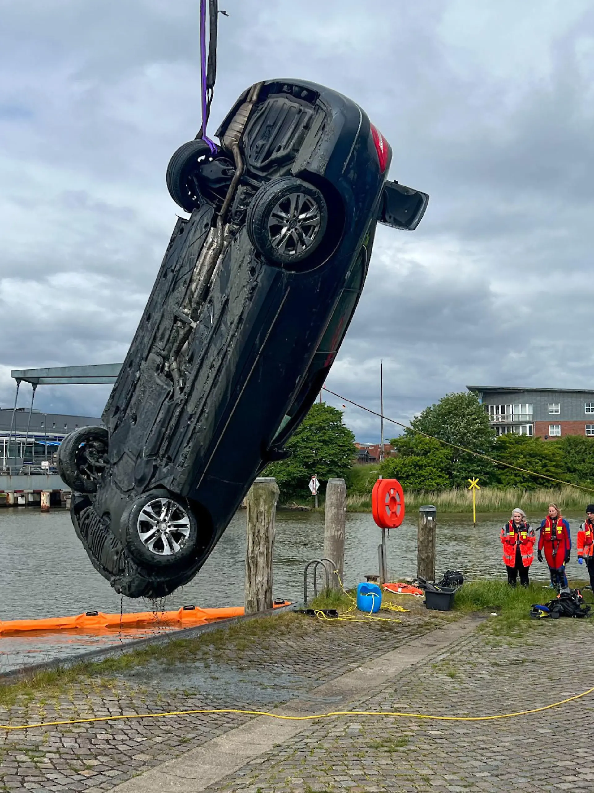dpatopbilder - 30.05.2022, Schleswig-Holstein, Husum: Einsatzkräfte ziehen mit einem Kran ein Auto aus dem Husumer Hafenbecken. Ein Auto mit zwei Insassen ist am Montag im Husumer Hafenbecken versunken - beide Menschen starben. Es handle sich um eine Frau und einen Mann, sagte ein Sprecher der Regionalleitstelle Nord am Abend. Zeugen hätten beobachtet, dass der Wagen einparken wollte, dann einen Satz nach vorne gemacht habe und ins Wasser gestürzt sei. Nach dem mutmaßlichen Unglück am Nachmittag seien sehr viele Notrufe eingegangen. Das Auto sei unterdessen aus dem Becken geholt worden. Foto: Benjamin Nolte/dpa +++ dpa-Bildfunk +++