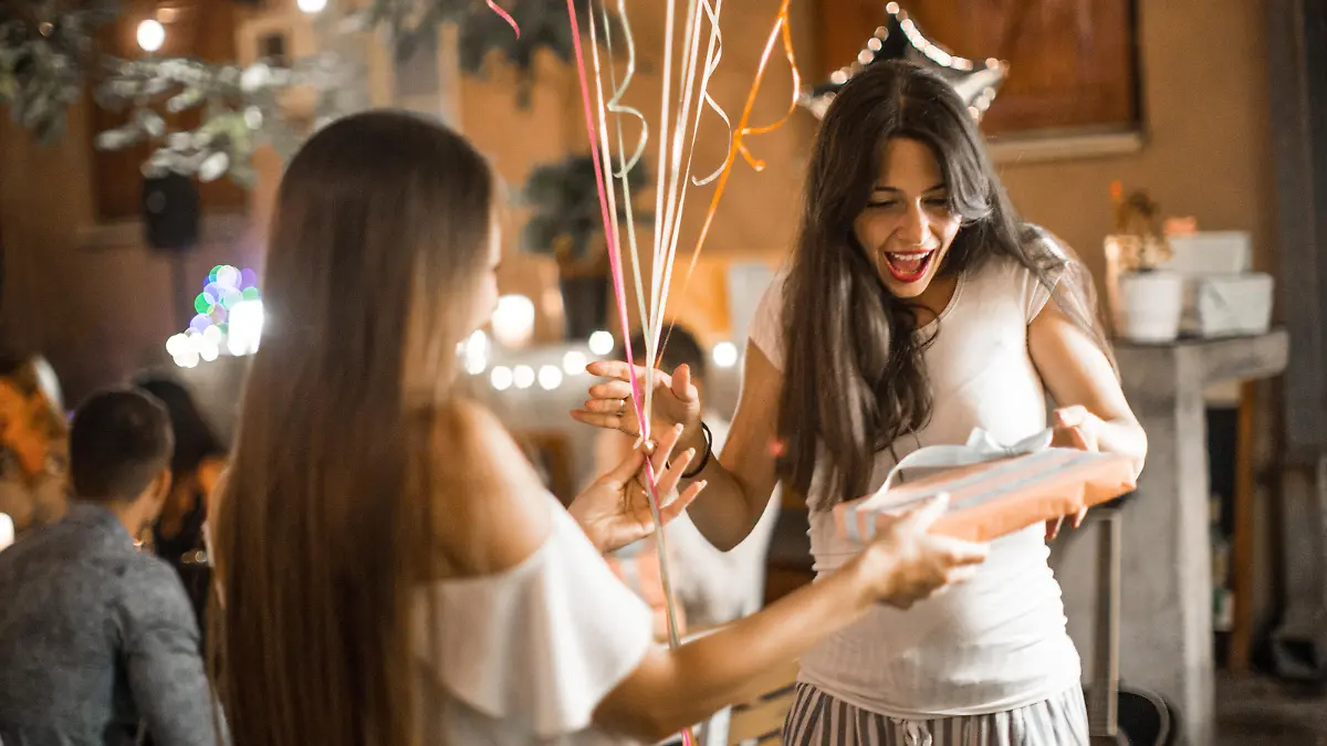 Woman welcoming guest on her birthday dinner party and receiving gifts