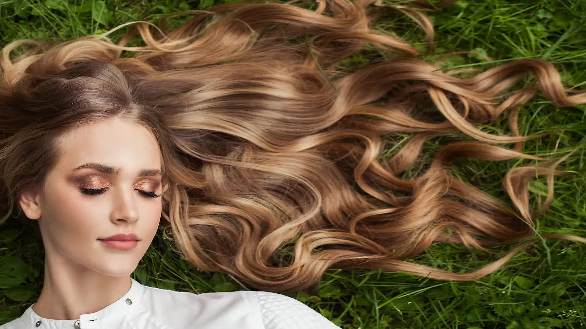 Beautiful woman with healthy curly hair relaxing on green grass outdoor, top view