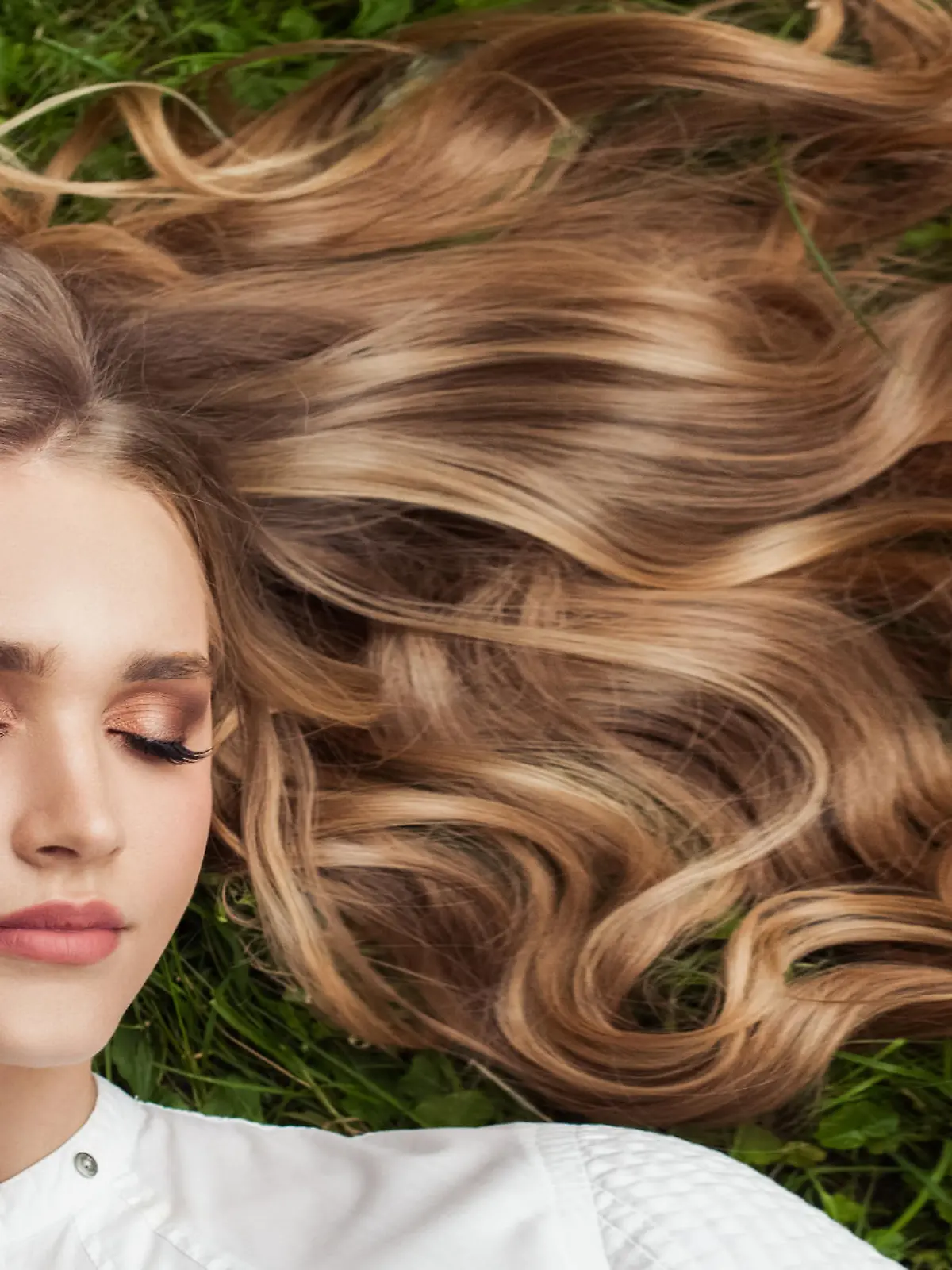 Beautiful woman with healthy curly hair relaxing on green grass outdoor, top view