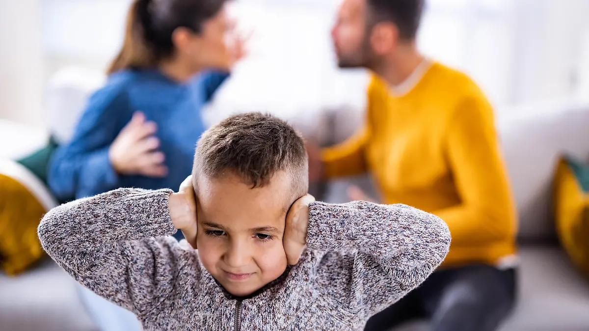 Small boy covering his ears while refusing to listen his parents arguing.