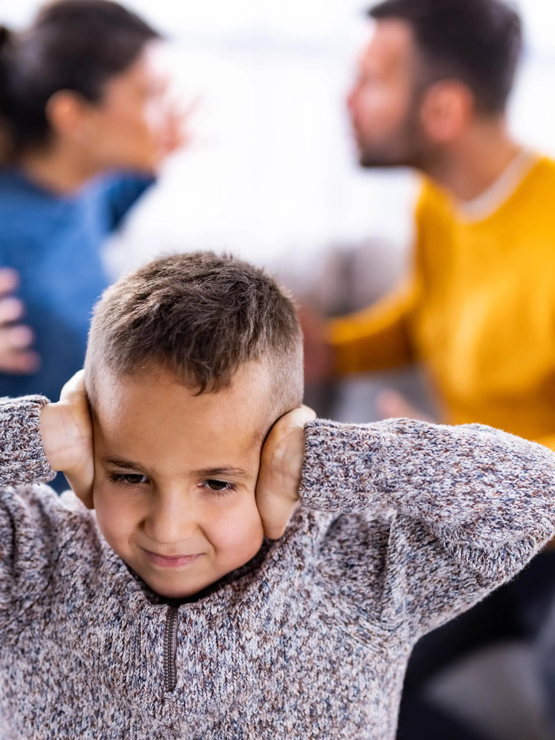 Small boy covering his ears while refusing to listen his parents arguing.