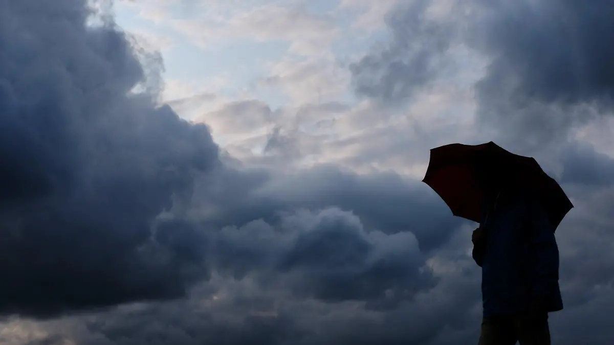 ARCHIV - 12.07.2019, Nordrhein-Westfalen, Duisburg: Ein Mann geht mit einem Regenschirm vor aufziehenden dunklen Wolken spazieren. (zu dpa: «Wetterdienst: Schwere Gewitter mit Starkregen im Südwesten möglich») Foto: Martin Gerten/dpa +++ dpa-Bildfunk +++