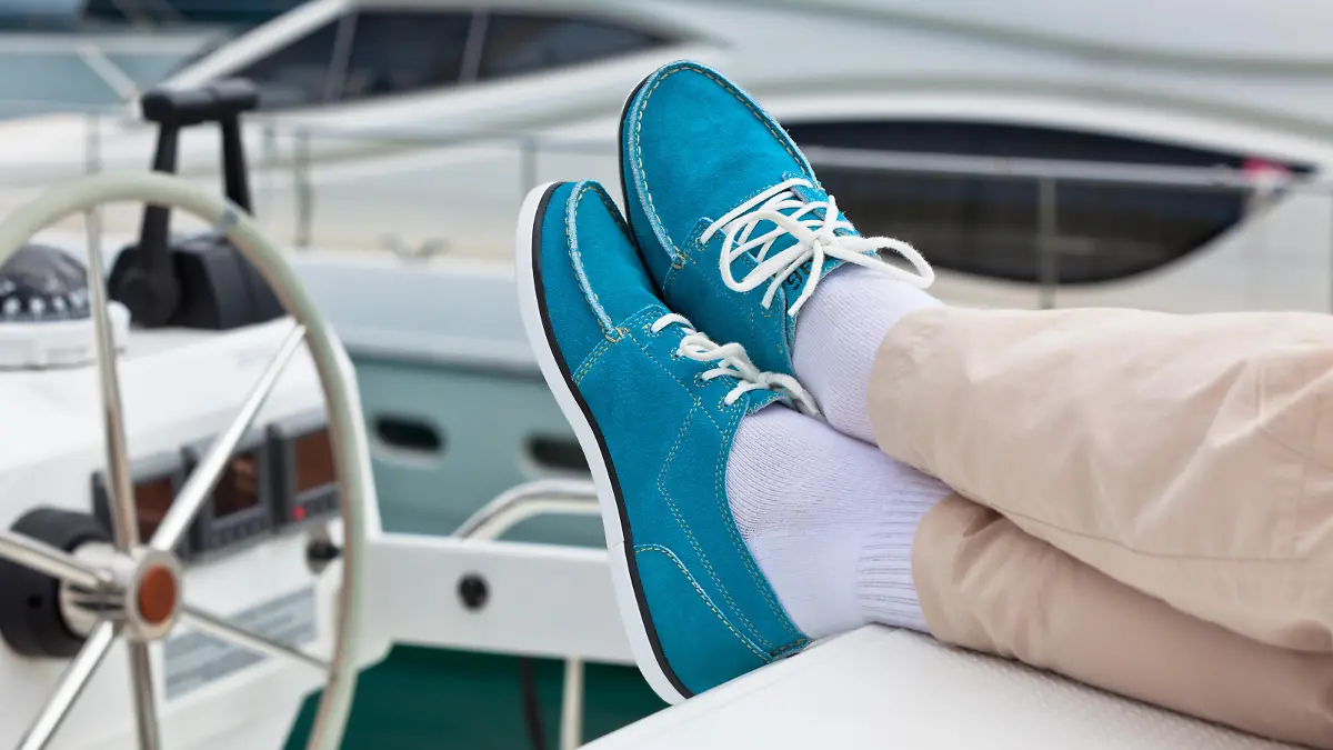 A pair of human legs in pants and bright blue topsiders on yacht deck background. Yachting