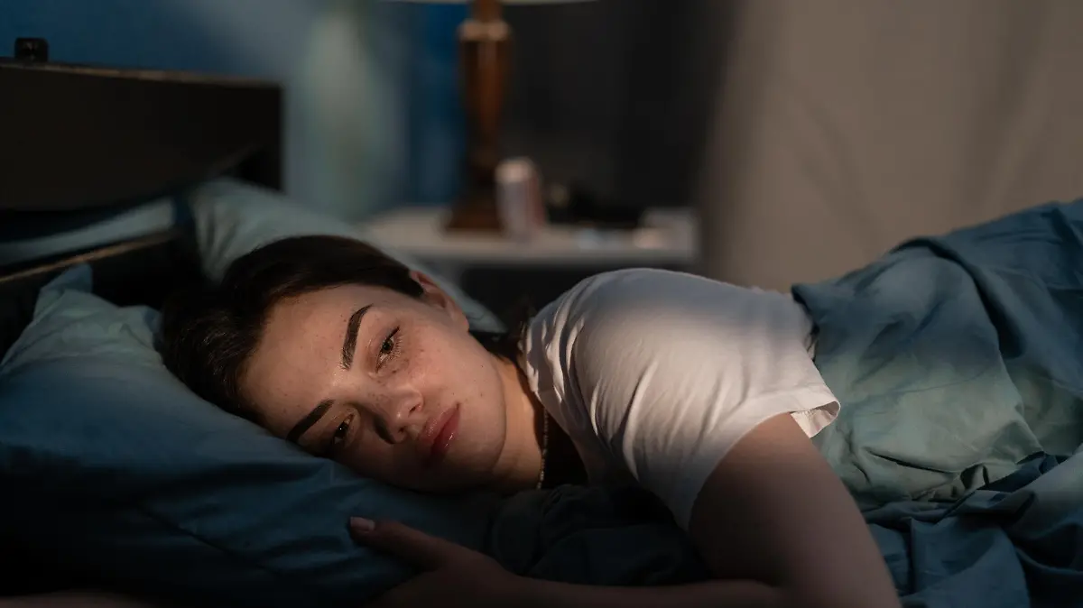 Young sad woman lying in bed late at night trying to sleep suffering insomnia. Girl in bed scared on nightmares looking worried and stressed. Sleeping disorder and insomnia concept