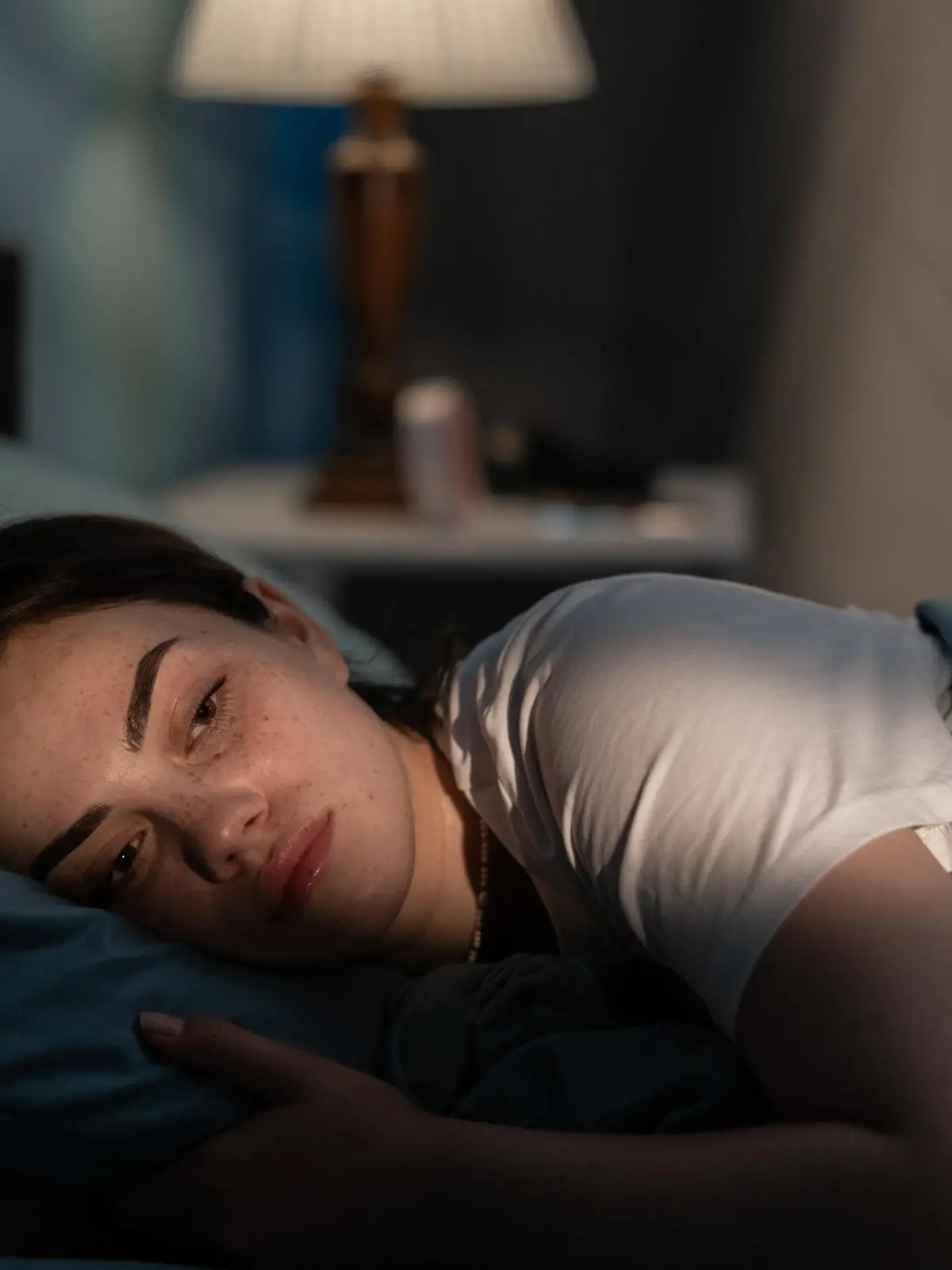 Young sad woman lying in bed late at night trying to sleep suffering insomnia. Girl in bed scared on nightmares looking worried and stressed. Sleeping disorder and insomnia concept