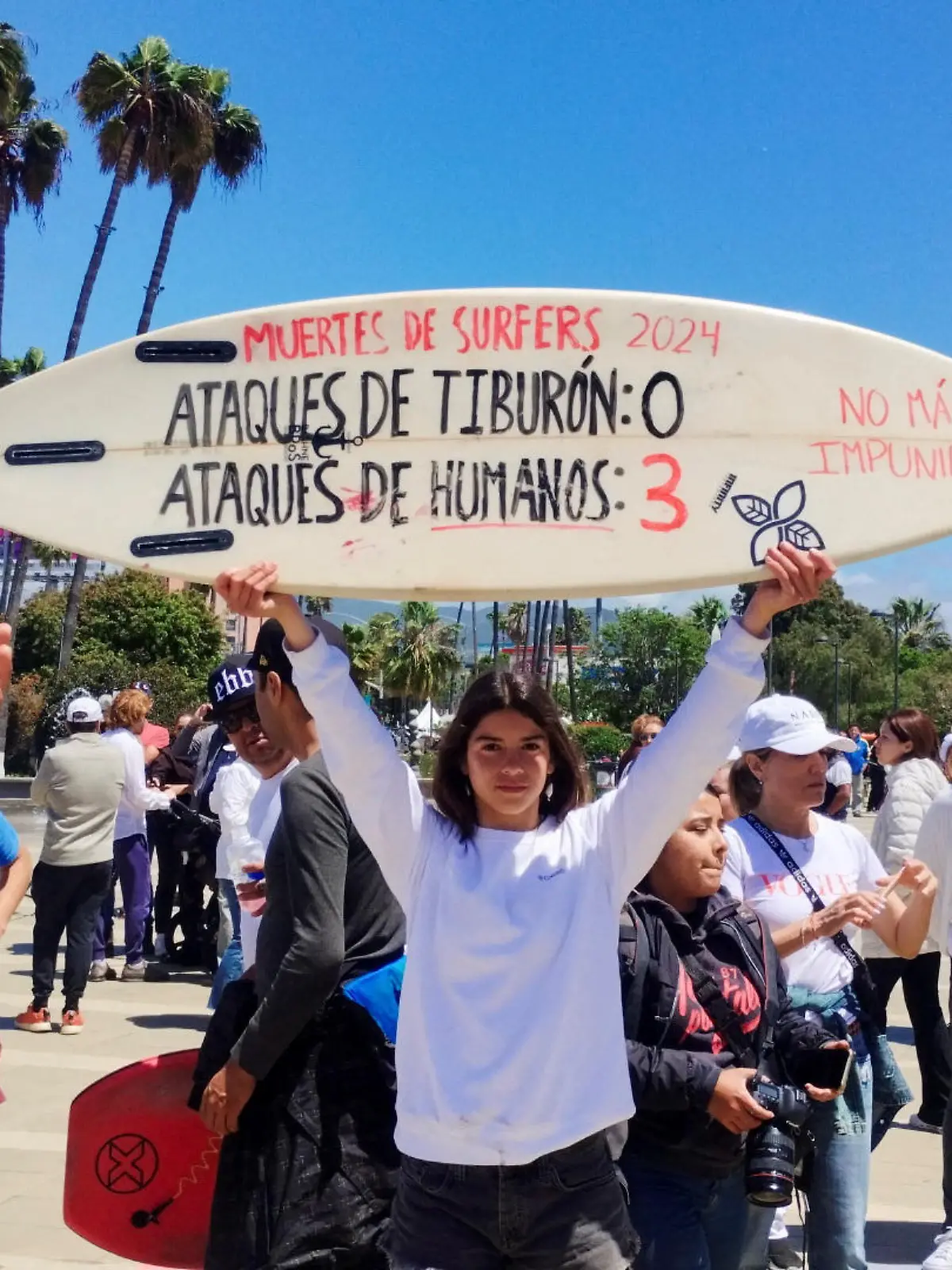 A woman holds a surfboard with the writing “Surfer deaths-Shark attacks: 0 and Human attacks: 3” during a protest as Mexican authorities confirmed U.S. and Australian tourists who went missing in northern Mexico last week are dead after their bodies were identified by their parents, in Ensenada, Mexico May 5, 2024.  REUTERS/Francisco Javier Cruz