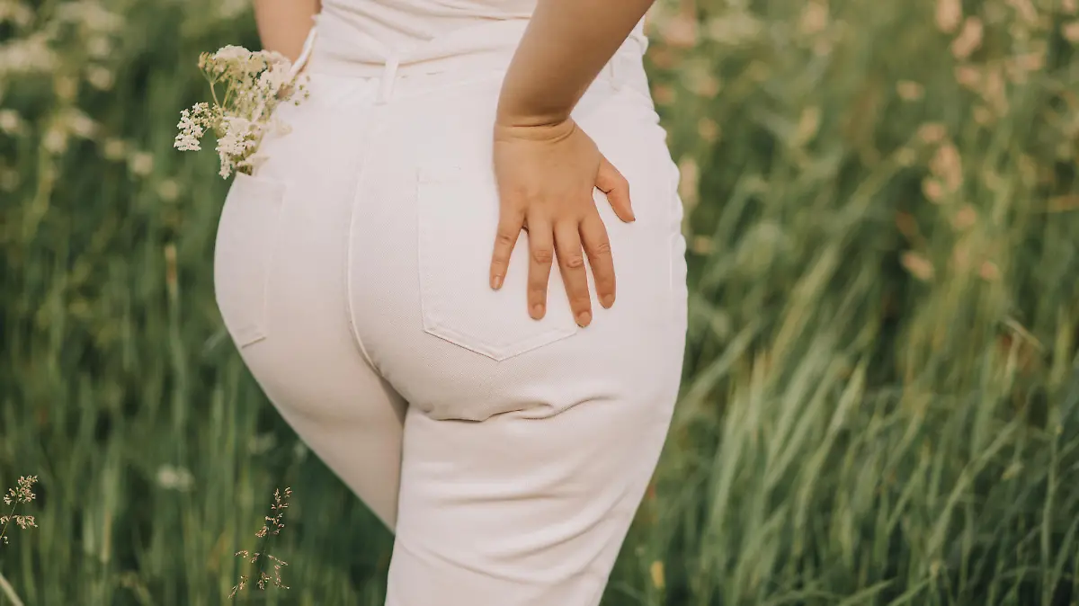 Closeup of a woman in white jeans on a blooming field background. Stylish look, fashion for curvy women, outdoor recreation.