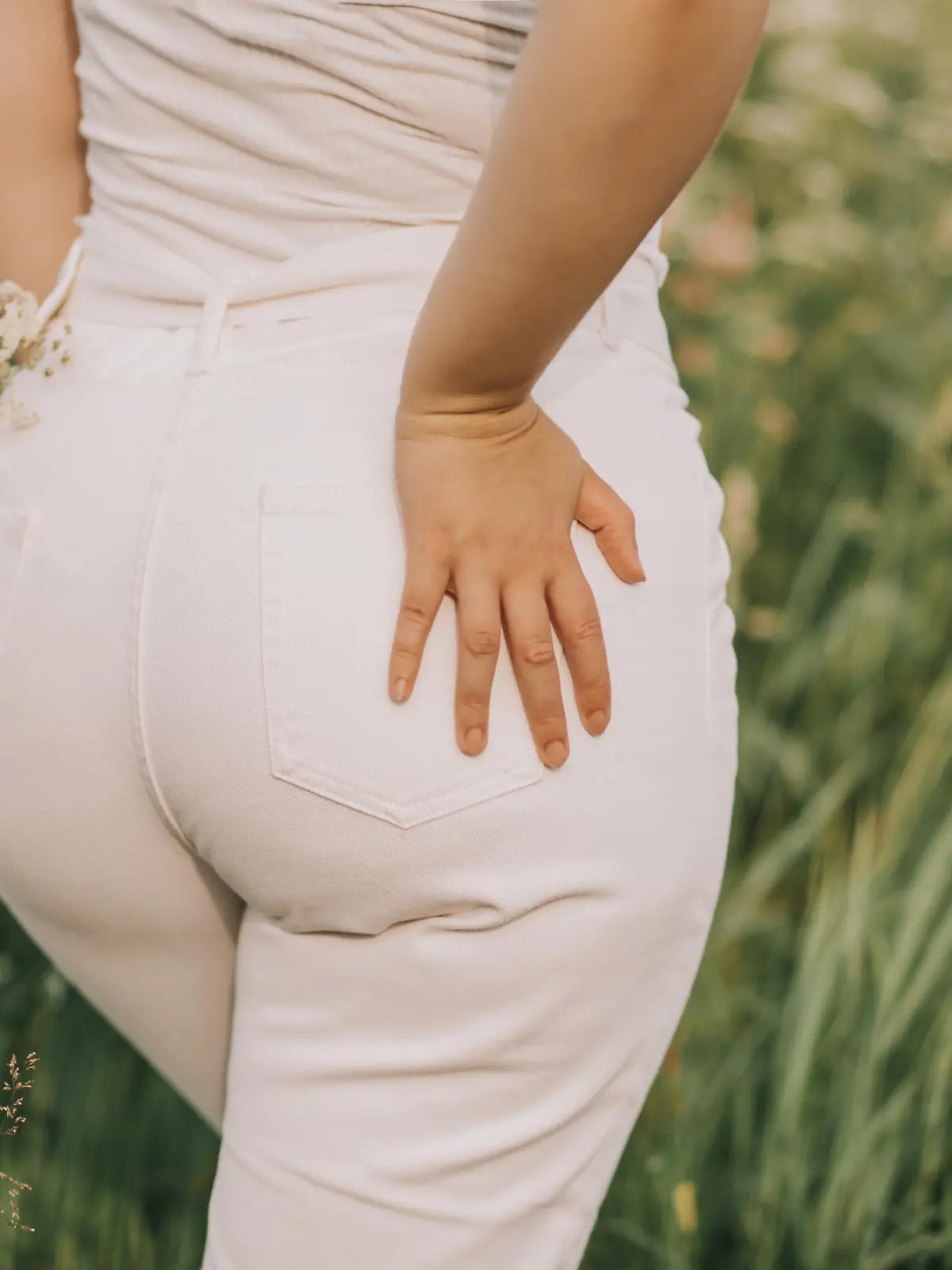 Closeup of a woman in white jeans on a blooming field background. Stylish look, fashion for curvy women, outdoor recreation.