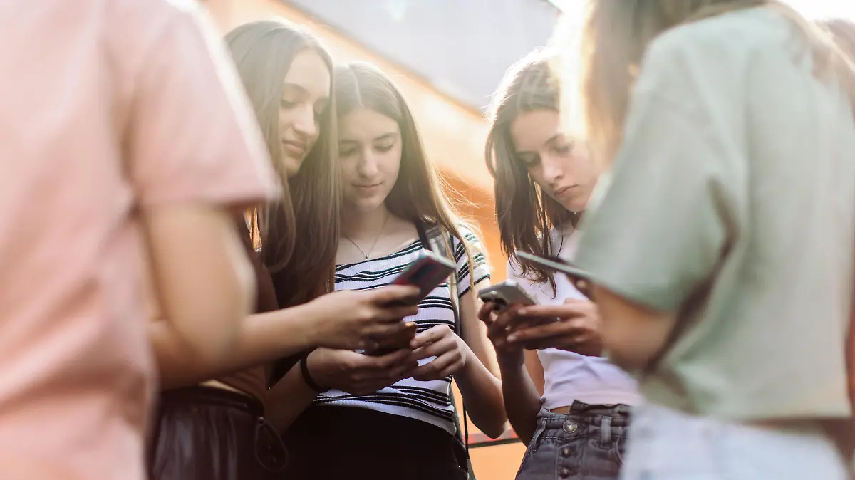 Group of teenage students standing in schoolyard and using mobile phones. They are very happy and playful.