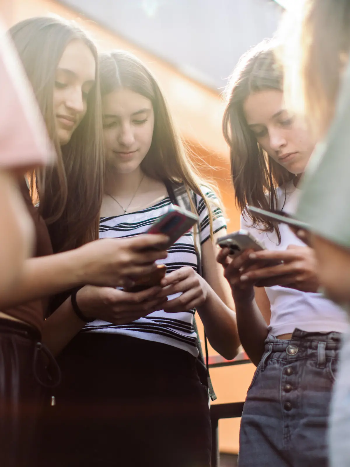 Group of teenage students standing in schoolyard and using mobile phones. They are very happy and playful.