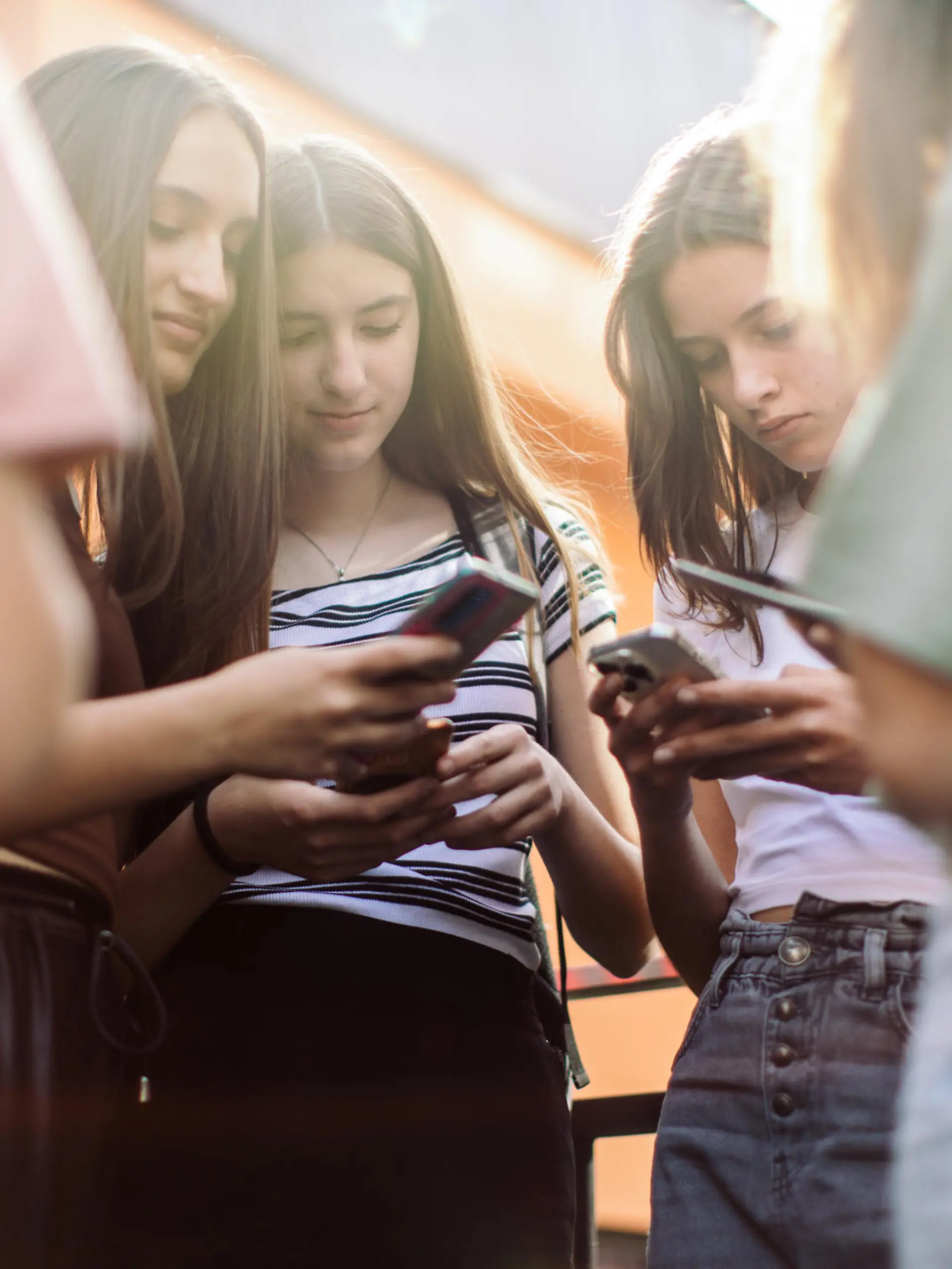 Group of teenage students standing in schoolyard and using mobile phones. They are very happy and playful.