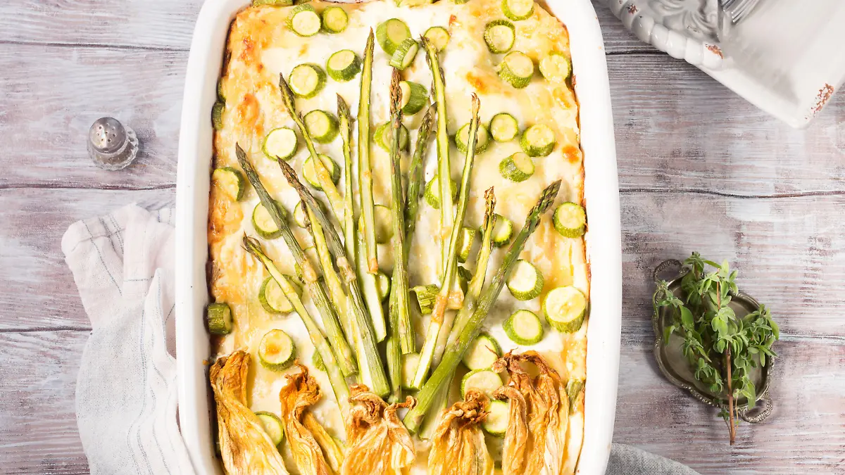 Home made asparagus lasagna casserole with zucchini, ricotta, mozzarella cheese and marjoram herb in a ceramic tin on wooden table. Rustic spring baked one plate food