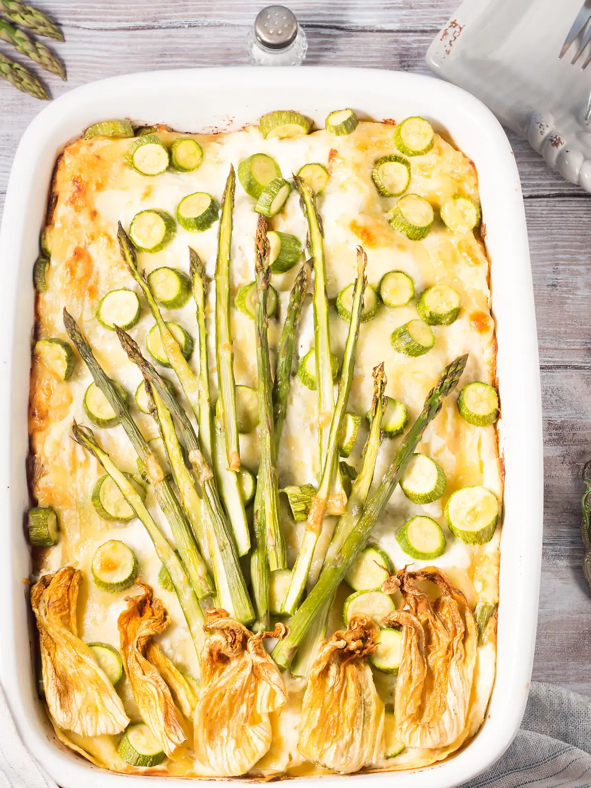 Home made asparagus lasagna casserole with zucchini, ricotta, mozzarella cheese and marjoram herb in a ceramic tin on wooden table. Rustic spring baked one plate food