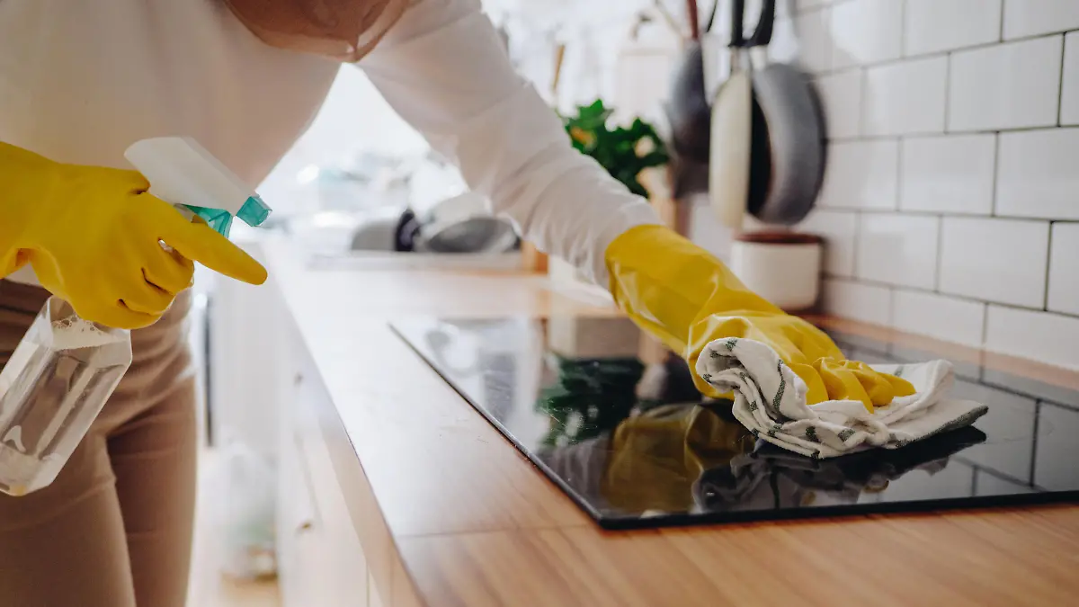 Young muslim woman cleaning modern cooking glass ceramic electric surface with sponge and detergent