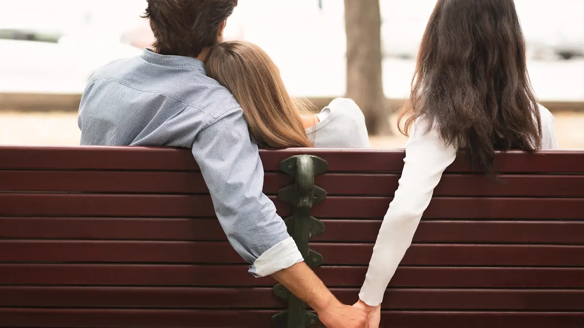 Love Triangle. Cheating Boyfriend Hugging Girlfriend Holding Hands With Her Girl Friend Sitting On Bench Together In Park Outdoor. Back-View