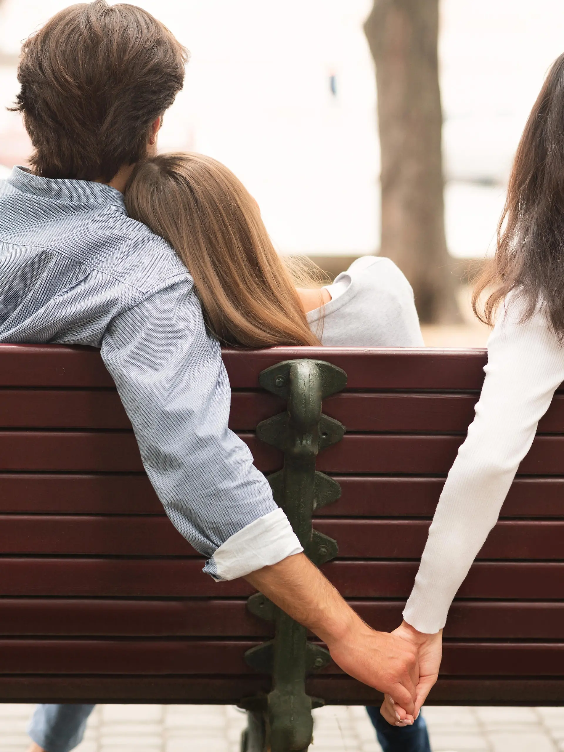 Love Triangle. Cheating Boyfriend Hugging Girlfriend Holding Hands With Her Girl Friend Sitting On Bench Together In Park Outdoor. Back-View