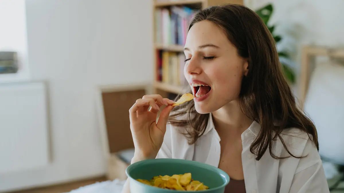 Enjoying crunchy chips. Woman has cravings for potato chips, eating with closed eyes, holding bowl. Enjoying crunchy chips. Woman has cravings for potato chips, eating with closed eyes, holding bowl full of crisps. model released