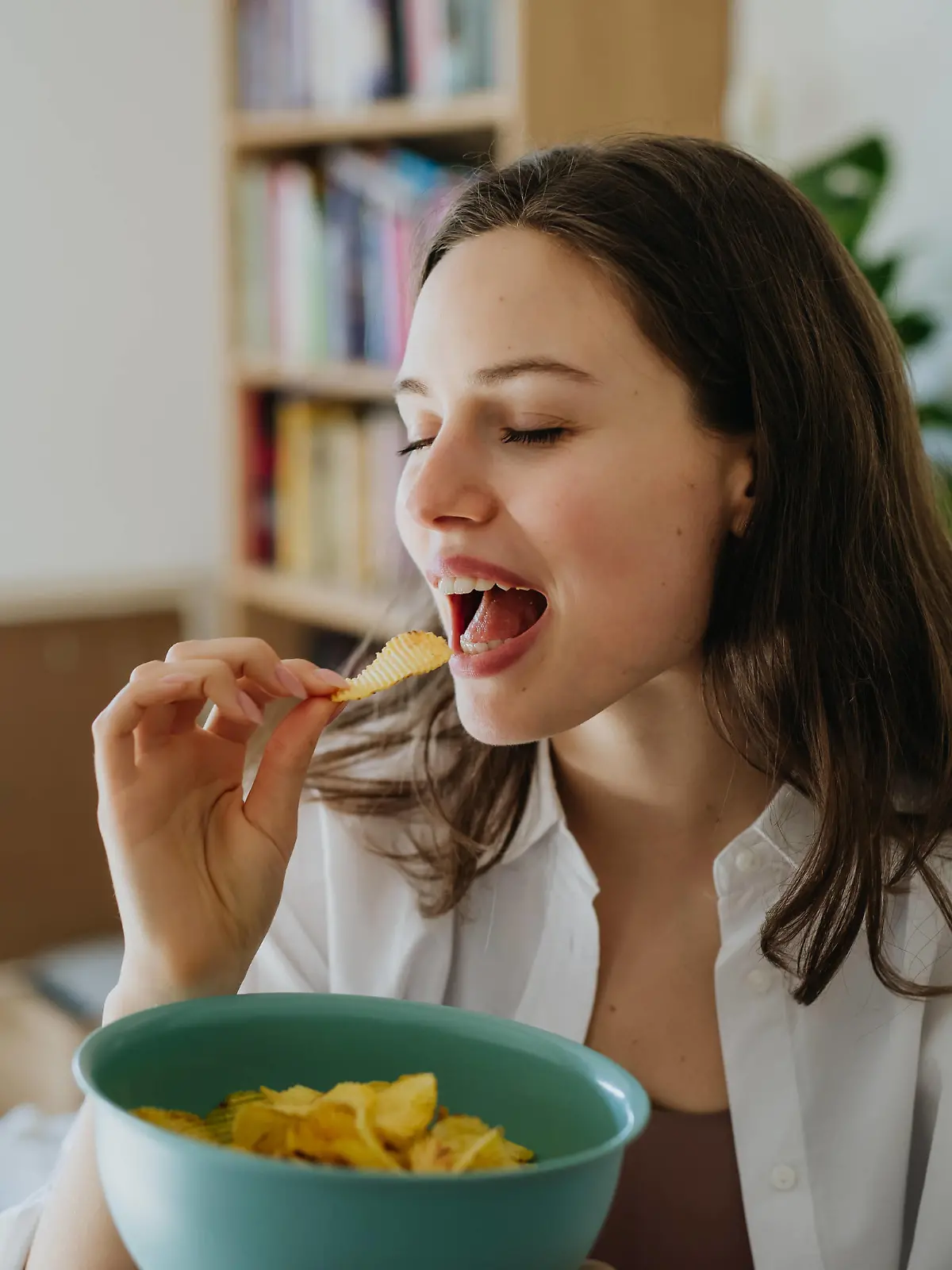 Enjoying crunchy chips. Woman has cravings for potato chips, eating with closed eyes, holding bowl. Enjoying crunchy chips. Woman has cravings for potato chips, eating with closed eyes, holding bowl full of crisps. model released
