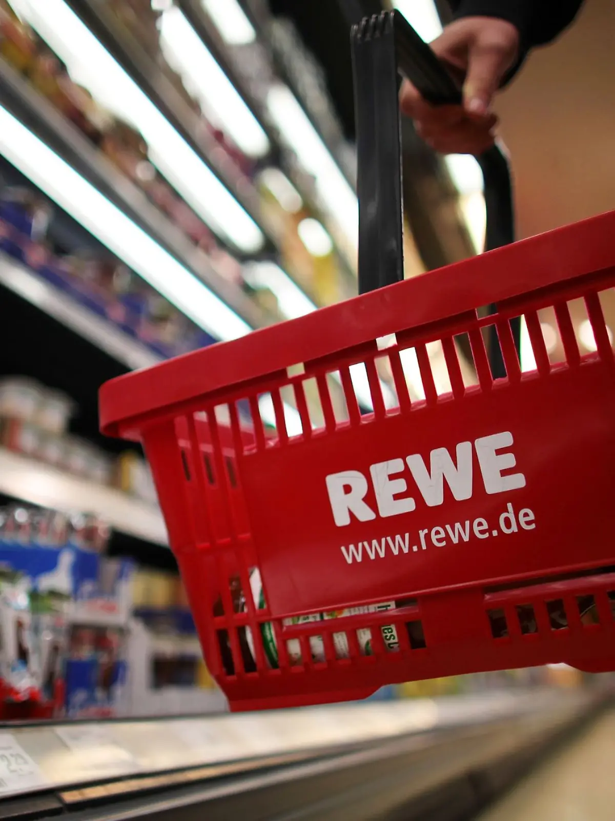 Ein Kunde geht in Köln in einem Rewe-Supermarkt mit einem Einkaufskorb am Kühlregal entlang.