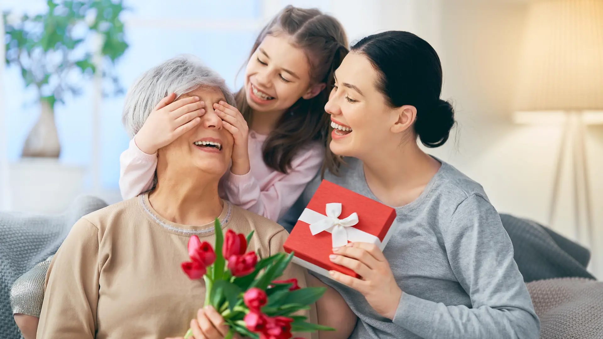 Happy women's day! Child daughter is congratulating mom and granny giving them flowers tulips. Grandma, mum and girl smiling and hugging. Family holiday and togetherness.