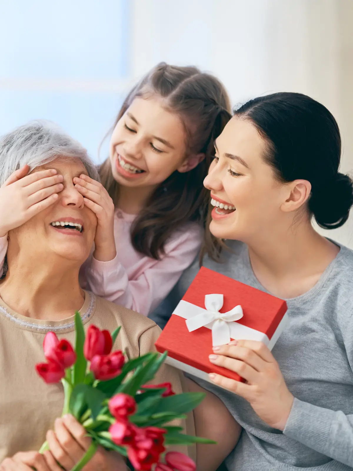                                 Happy women's day! Child daughter is congratulating mom and granny giving them flowers tulips. Grandma, mum and girl smiling and hugging. Family holiday and togetherness.