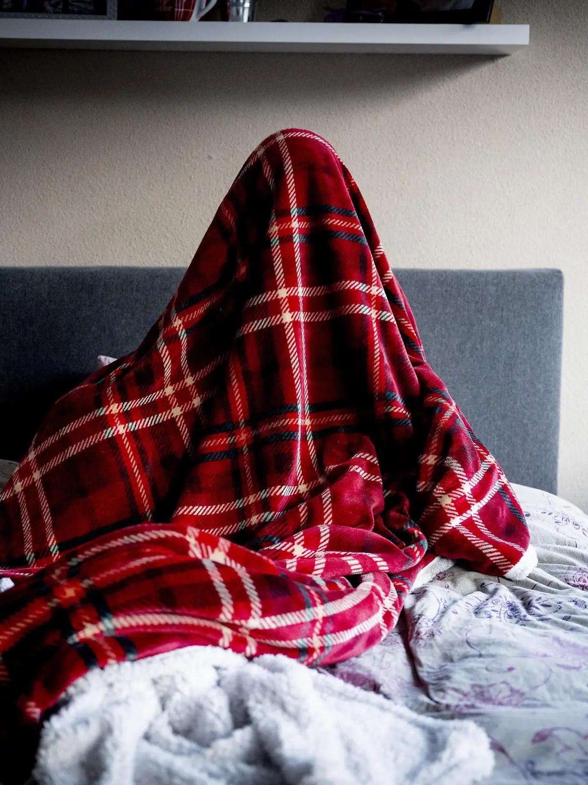 Ein Kind sitzt unter einer Decke auf einem Bett.
