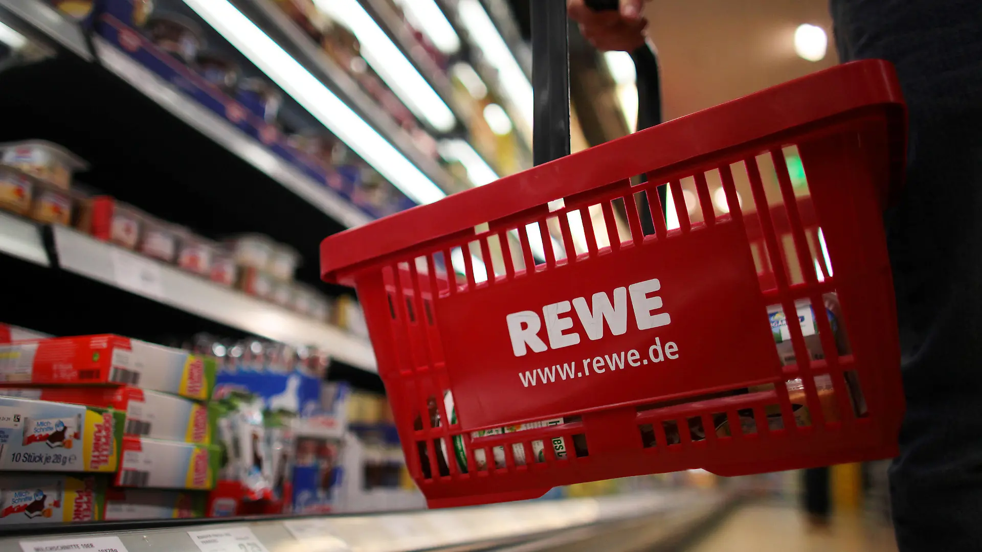 Ein Kunde geht in Köln in einem Rewe-Supermarkt mit einem Einkaufskorb am Kühlregal entlang