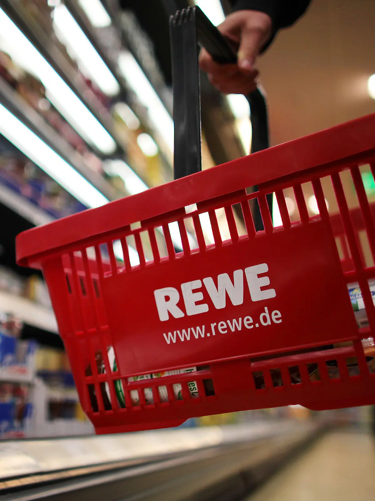 Ein Kunde geht in Köln in einem Rewe-Supermarkt mit einem Einkaufskorb am Kühlregal entlang