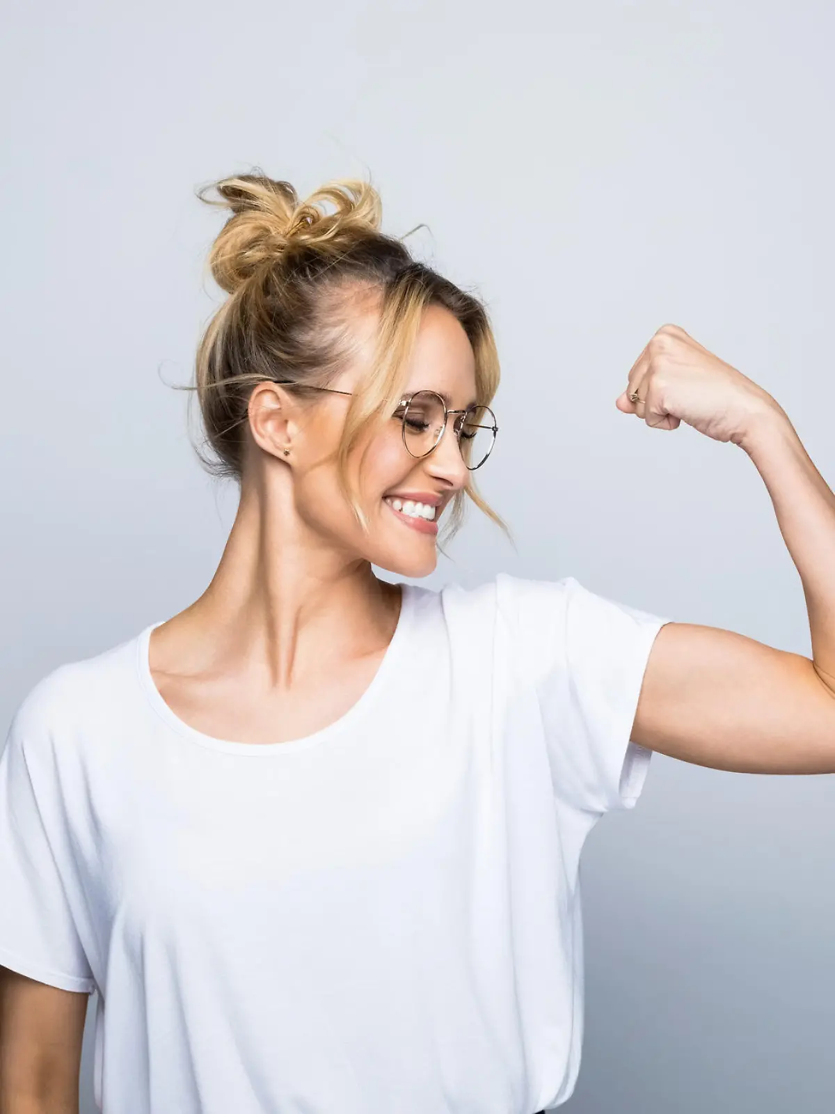 Happy beautiful woman flexing muscle while standing against gray background
