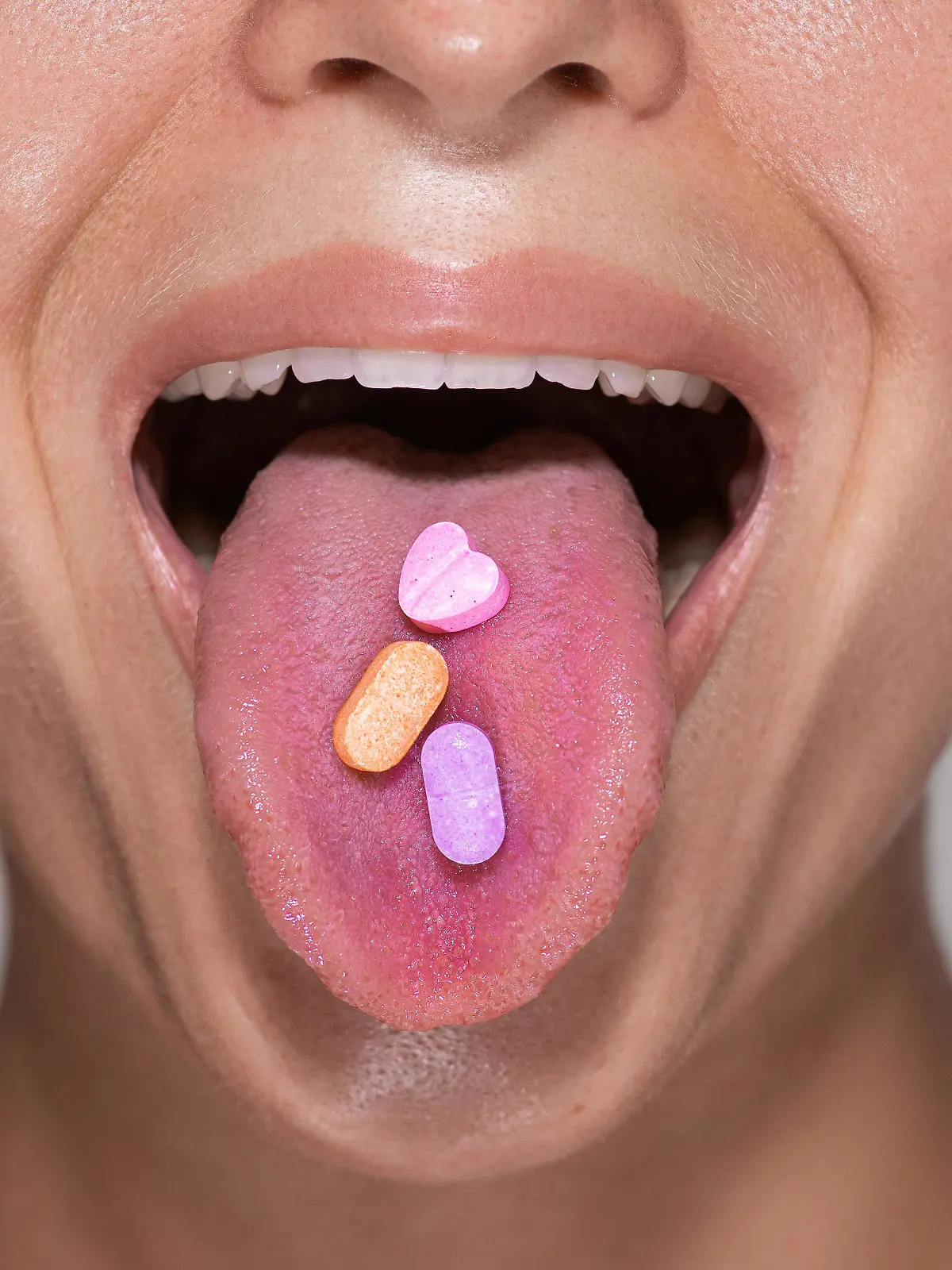 Closeup shot of a bottom part of a young female face with colorful pills on her tongue. || Modellfreigabe vorhanden