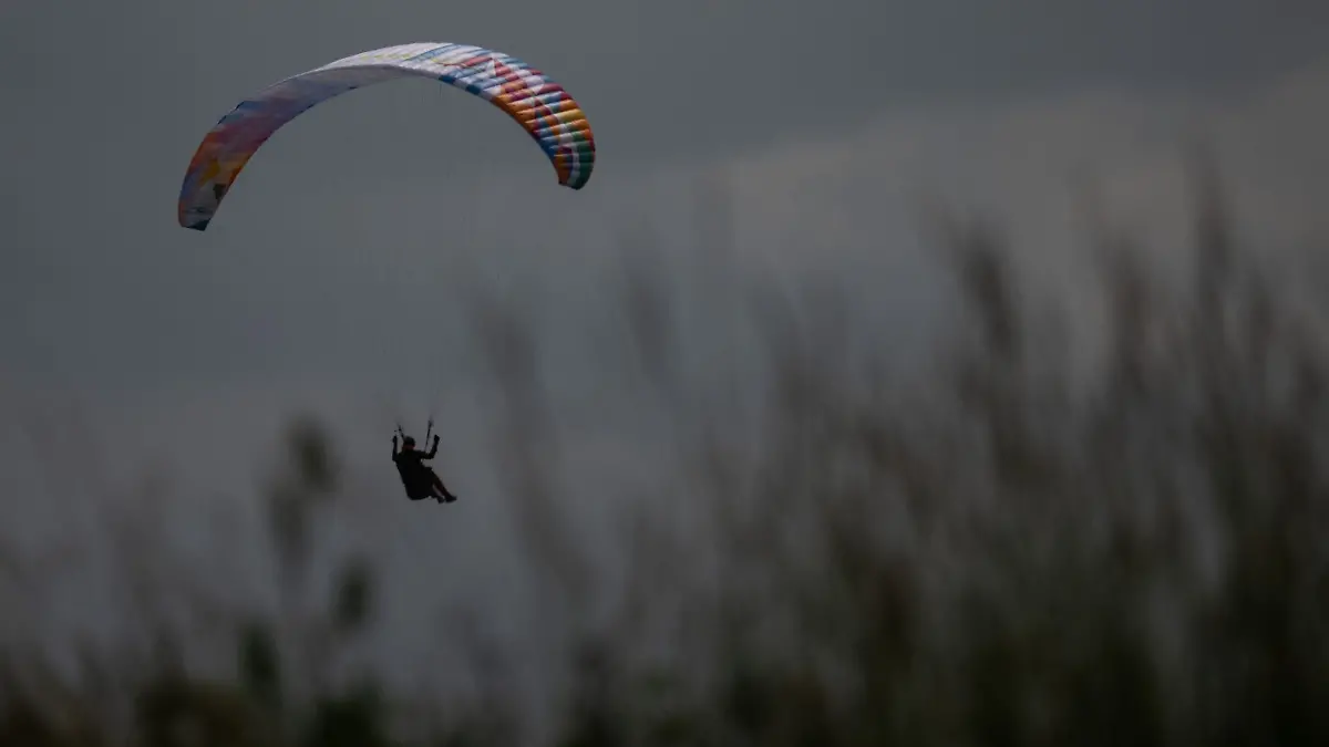 Ein Gleitschirmflieger wird von der Sonne angeschienen während er in einer Wiese landet.