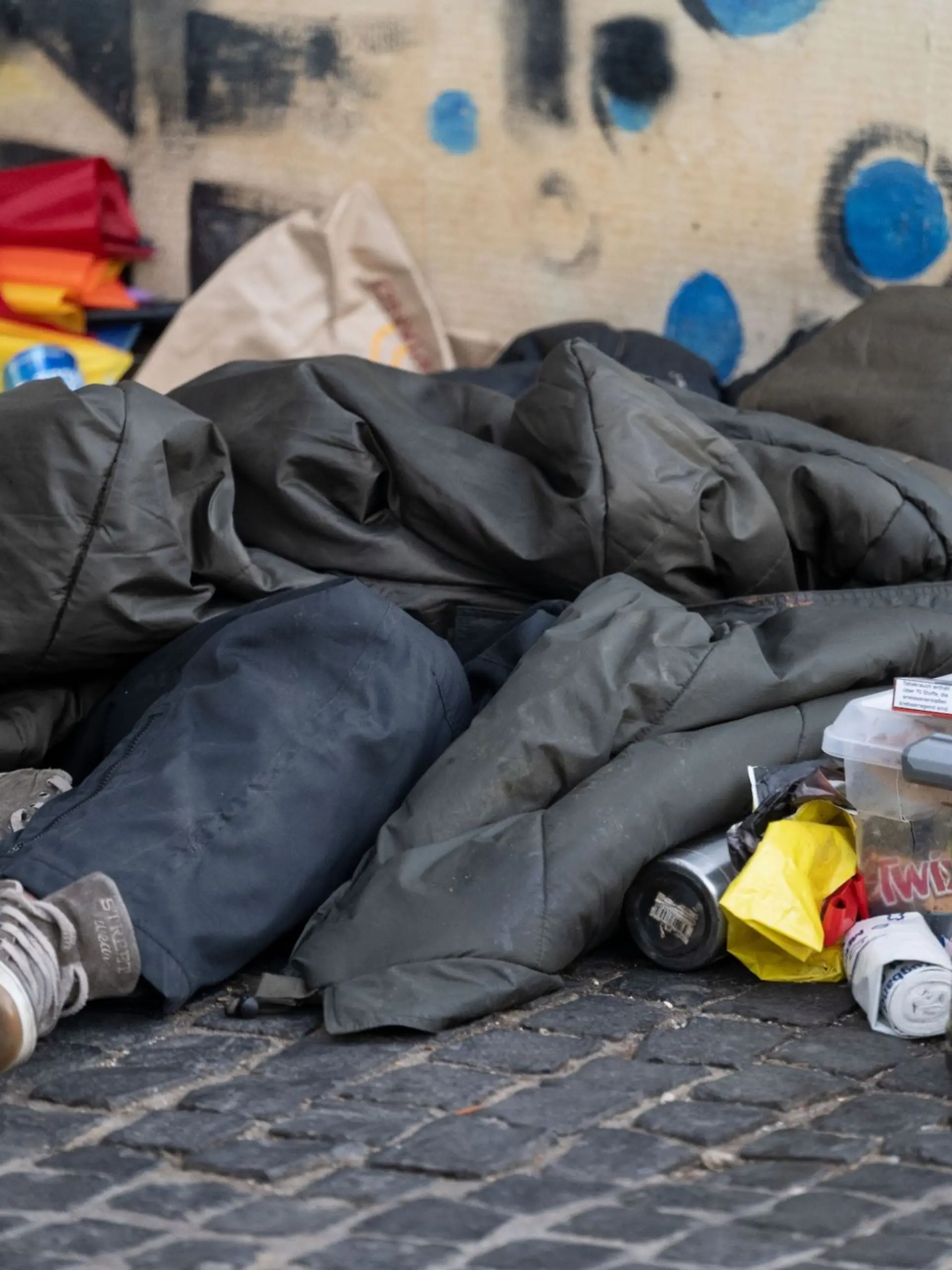 Eine Person liegt in der Innenstadt unter einem Schlafsack.