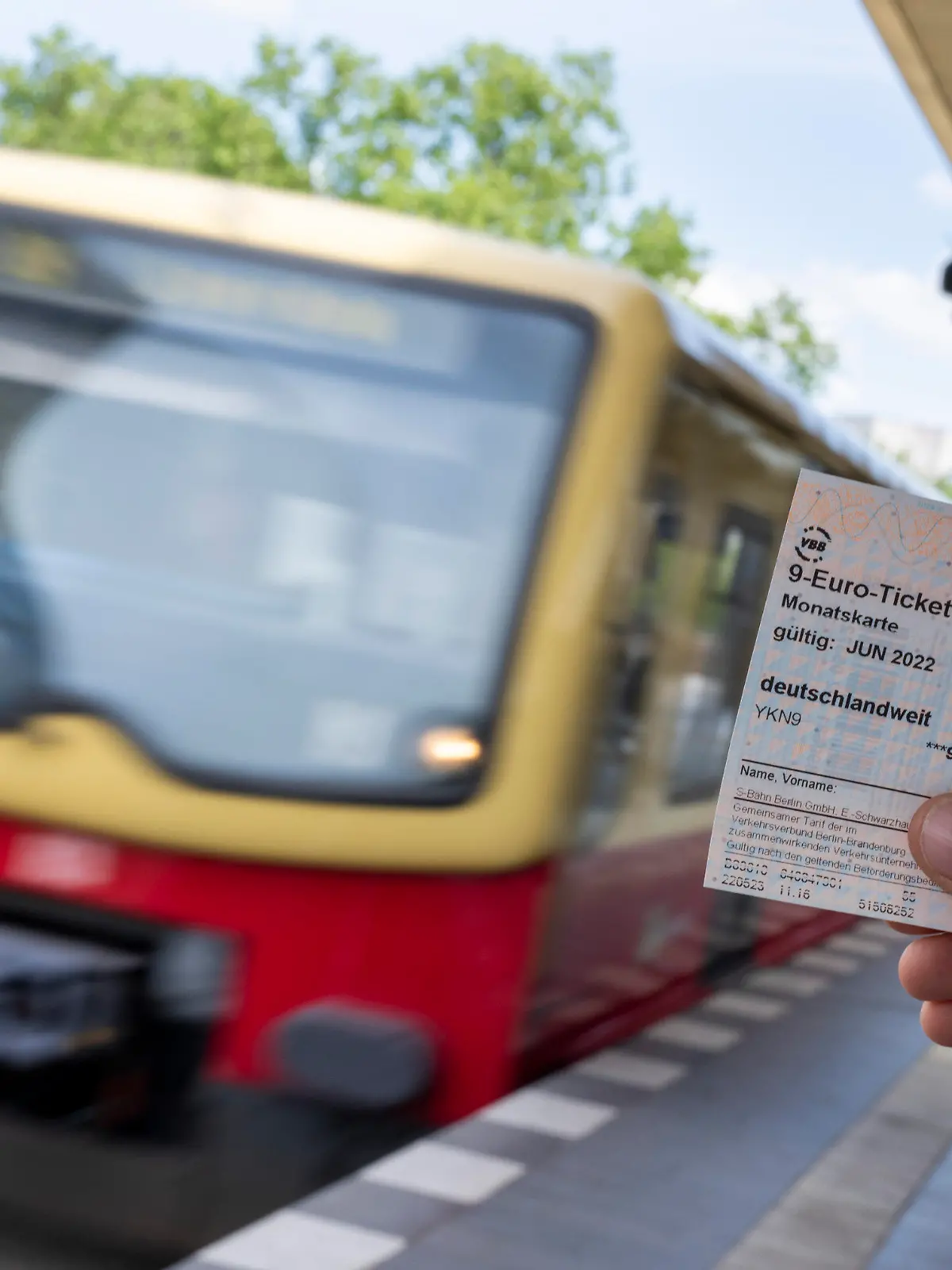 ILLUSTRATION - 23.05.2022, Berlin: Ein 9-Euro-Ticket ist vor dem Hintergrund einer einfahrenden S-Bahn zu sehen (gestelltes Foto). Die Deutsche Bahn und zahlreiche Verkehrsverbünde beginnen mit dem Verkauf des 9-Euro-Monatstickets. Mit dem Monatsticket können die Fahrgäste im Juni, Juli und August für jeweils 9 Euro bundesweit im öffentlichen Nah- und Regionalverkehr fahren. Foto: Monika Skolimowska/dpa +++ dpa-Bildfunk +++