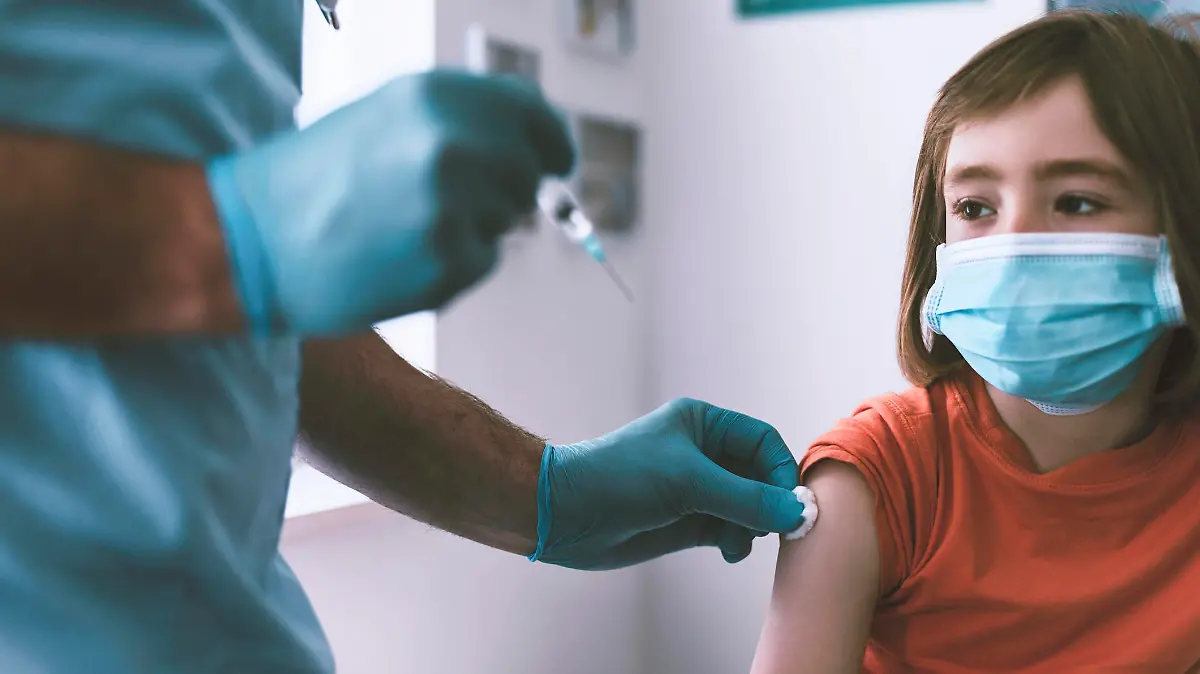 Doctor vaccinating a little boy wearing protective face mask . Doctor wearing protective workwear injecting vaccine into patient's arm.