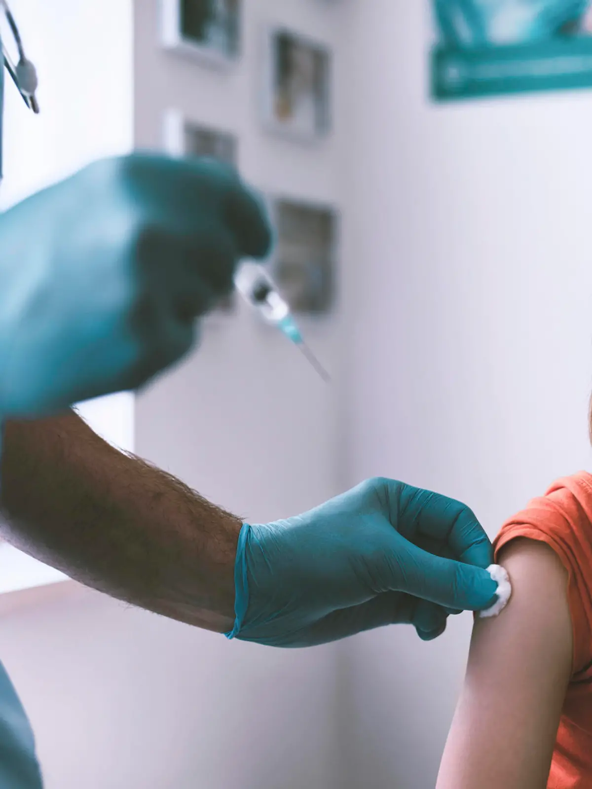 Doctor vaccinating a little boy wearing protective face mask . Doctor wearing protective workwear injecting vaccine into patient's arm.