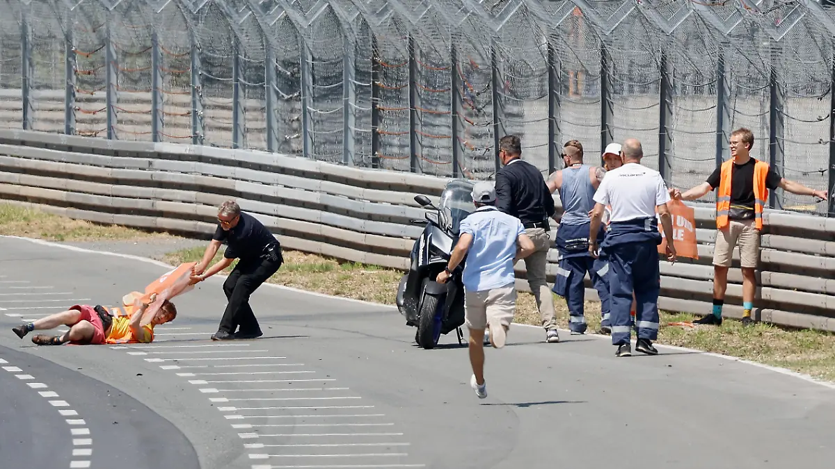 Streckenposten zerren einen Aktivisten der Letzten Generation mit Protestbanner in der Hand von der Fahrbahn, während ein Aktivist am Sicherheitszaun klebt. Am Wochenende findet das 80. Internationale ADAC Norisring Speedweekend statt.