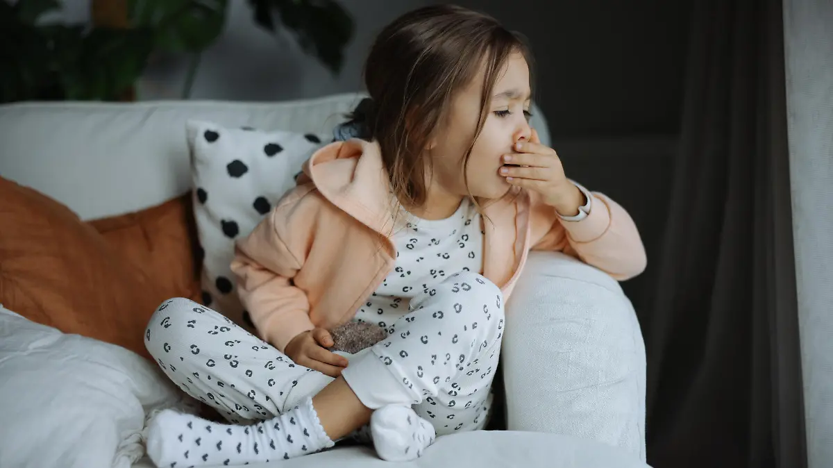 Poor, unfortunate little brunette preschooler child, girl in pajamas coughing, lying in soft bed. Sore throat, angina