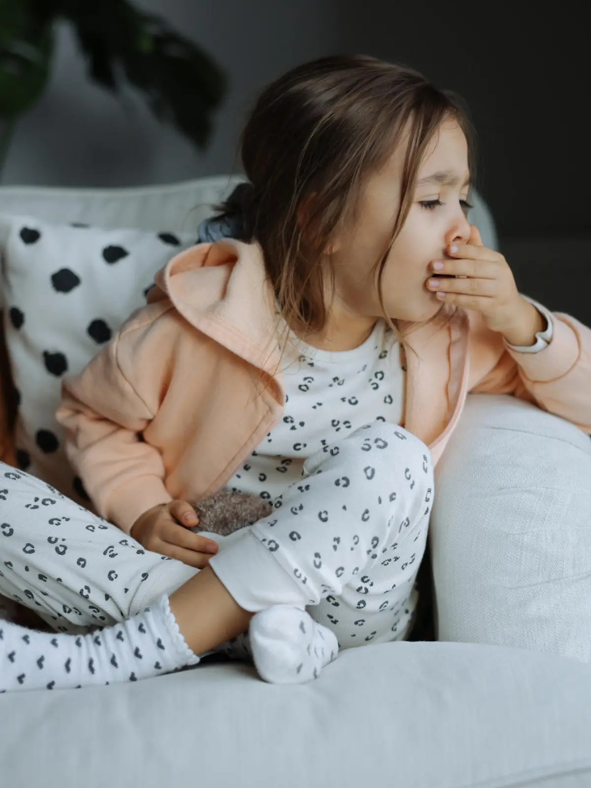 Poor, unfortunate little brunette preschooler child, girl in pajamas coughing, lying in soft bed. Sore throat, angina