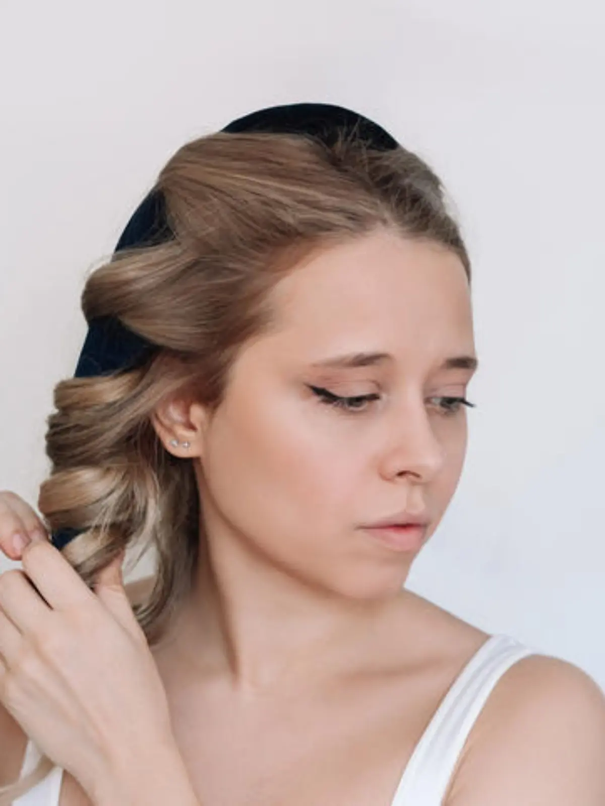 Heatless curl. A young attractive caucasian blonde woman removing soft curler from the hair on a light background. Healthy hair styling, no heating, no damage. A girl twisting curls around the rim