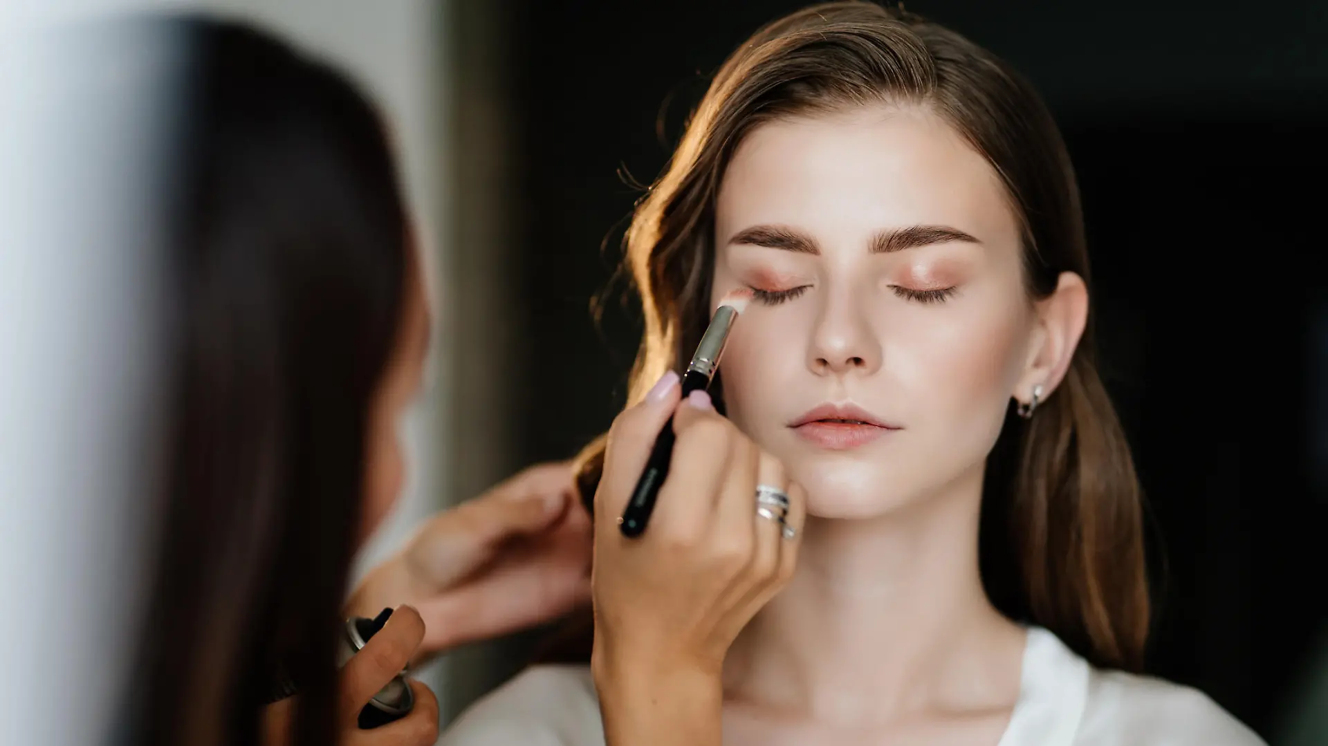 A beautiful young woman with long hair doing makeup for a wedding or photo shoot. the work of a make-up artist. the morning of the bride. decorative cosmetics.