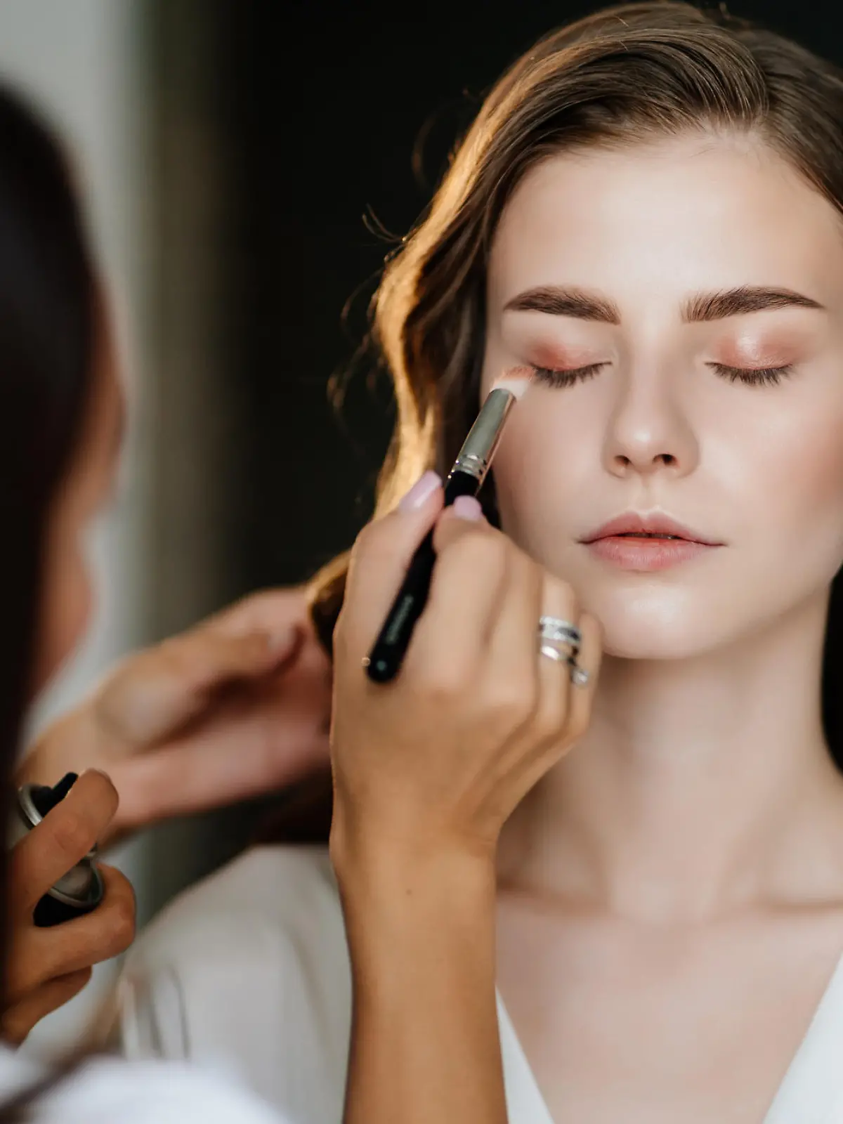 A beautiful young woman with long hair doing makeup for a wedding or photo shoot. the work of a make-up artist. the morning of the bride. decorative cosmetics.