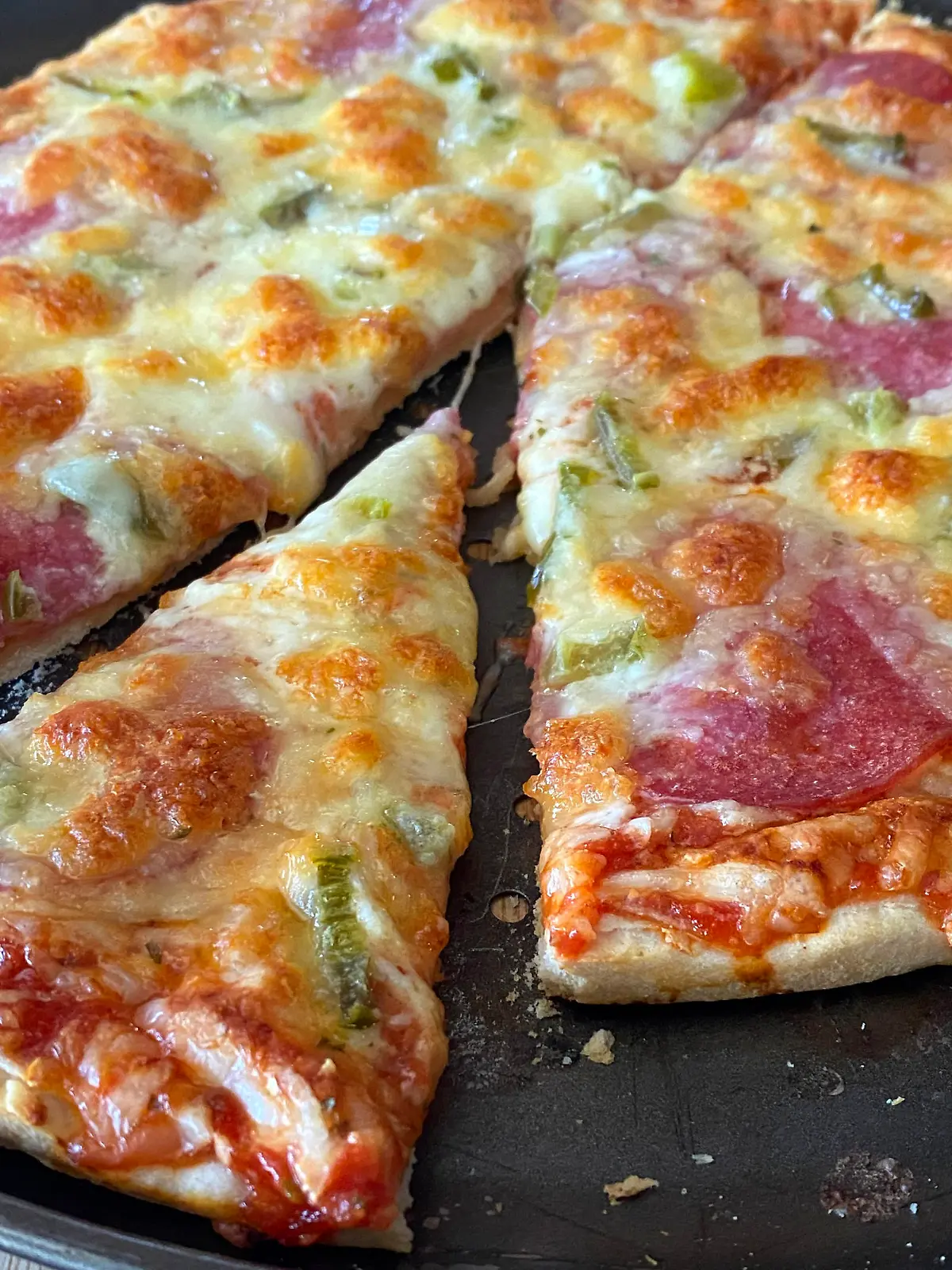 Angeschnittene, aufgebackene Tiefkuehlpizza mit viel Kaese und Salami auf einem Pizzablech,das gerade aus dem Backofen genommen wurde