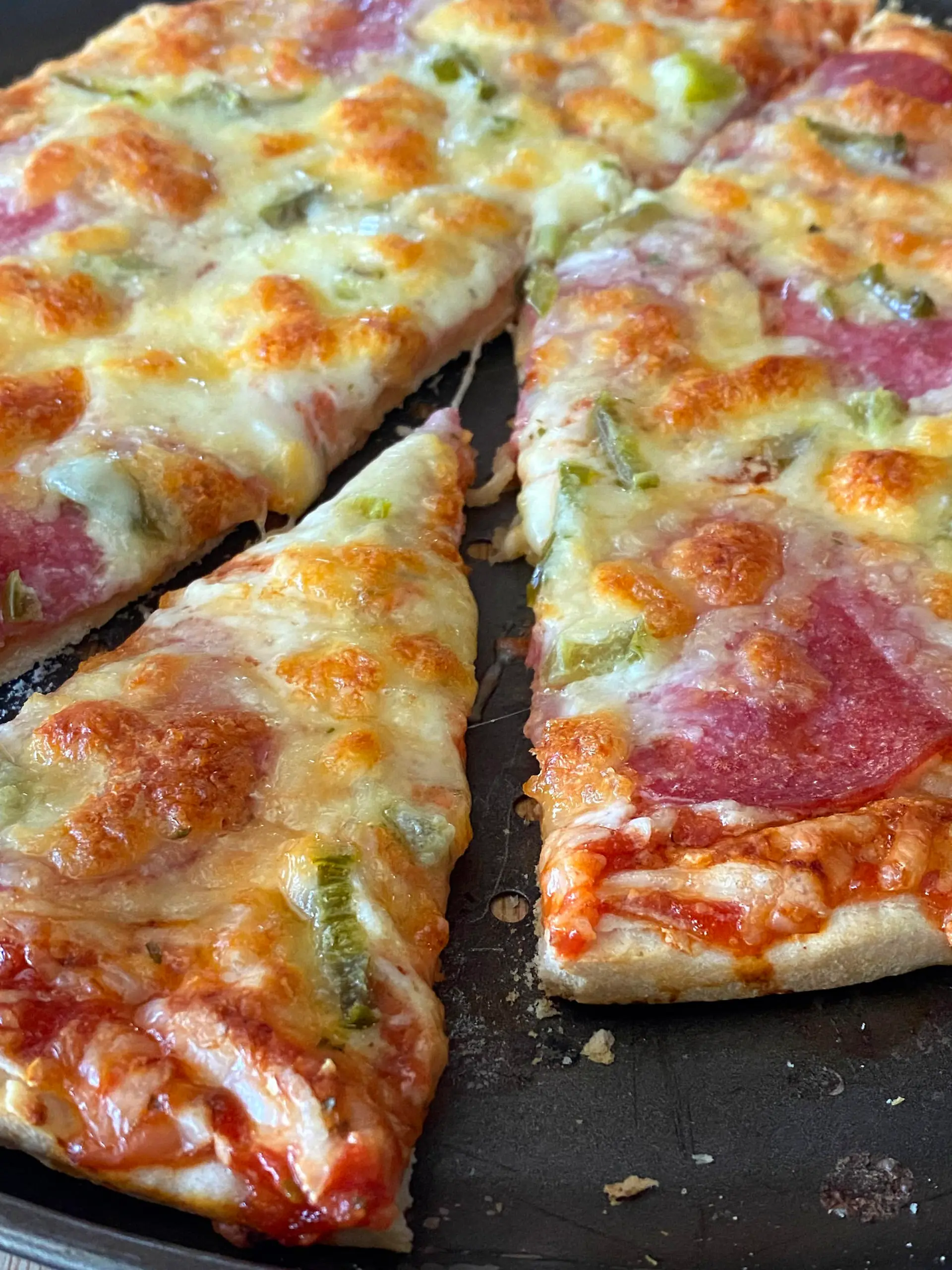 Angeschnittene, aufgebackene Tiefkuehlpizza mit viel Kaese und Salami auf einem Pizzablech,das gerade aus dem Backofen genommen wurde