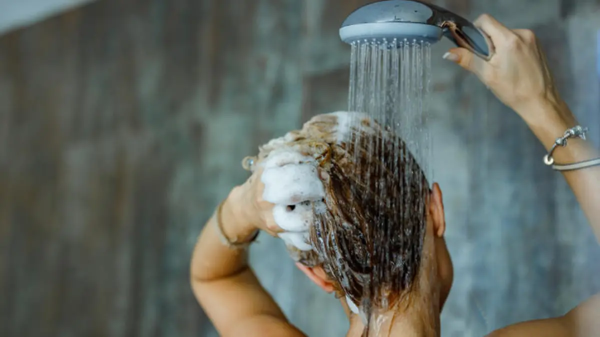 Back view of a woman washing her hair with a shampoo in bathroom. Copy space.