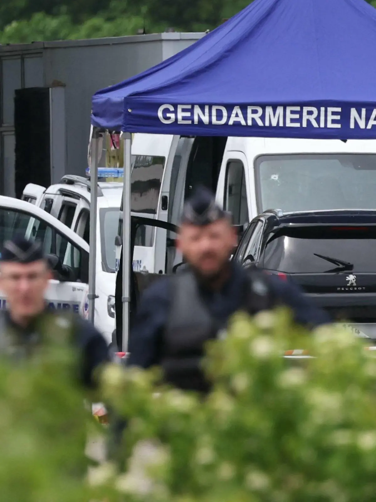 14.05.2024, Frankreich, Incarville: Ein Gerichtsmediziner arbeitet, während Polizisten am Ort eines Rammangriffs patrouillieren, der sich am späten Vormittag an einer Mautstelle in Incarville in der nordfranzösischen Region Eure ereignete. Bei einem Überfall auf einen Gefangenentransport im Norden Frankreichs seien Polizisten getötet und weitere verletzt worden. Foto: Alain Jocard/AFP/dpa +++ dpa-Bildfunk +++