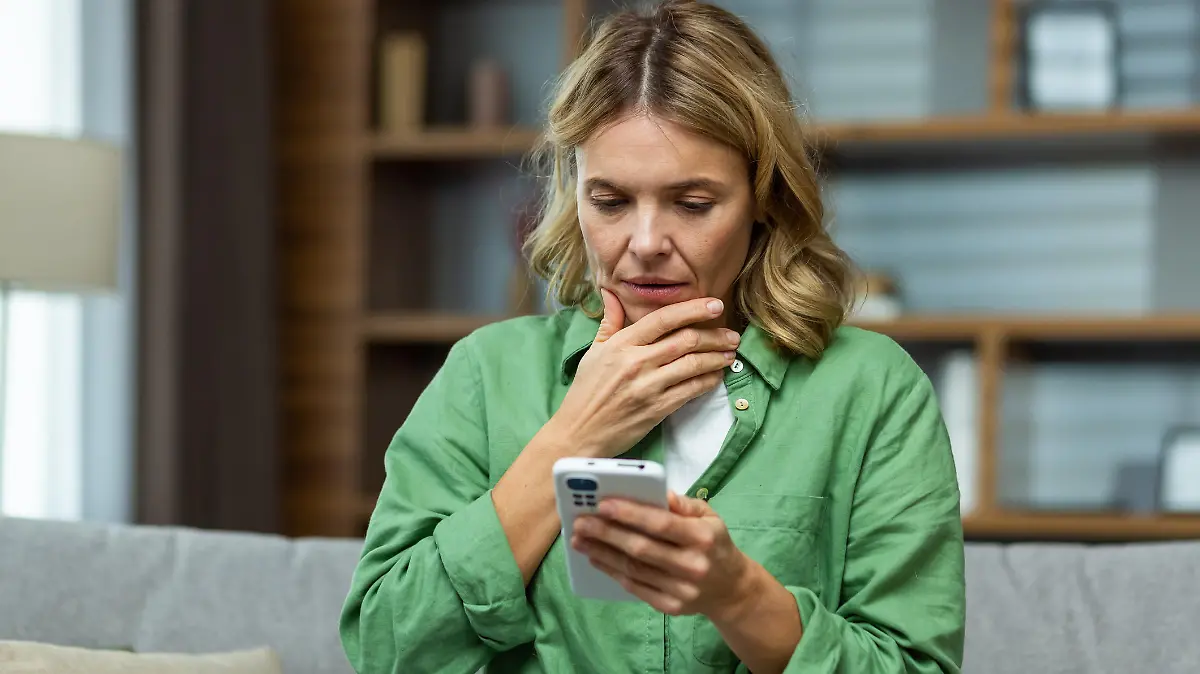Close-up photo. Worried senior woman mother sitting on sofa at home and holding phone. Worries about children, writes and sends messages, calls, searches, waits at home.