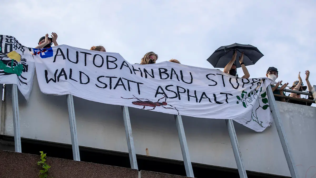 07.07.2023, Hessen, Frankfurt/Main: Klimaaktivisten stehen auf einem Parkhaus im Stadtteil Sachsenhausen hinter einem Banner mit der Aufschrift "Autobahnbau stoppen - Wald statt Asphalt". In Frankfurt haben Aktivisten der Klimaschutzbewegung Fridays for Future während einer Demonstration in der Innenstadt am Freitagnachmittag ein Parkhaus besetzt. Das teilte die Gruppe am Freitagabend mit. Foto: Helmut Fricke/dpa +++ dpa-Bildfunk +++