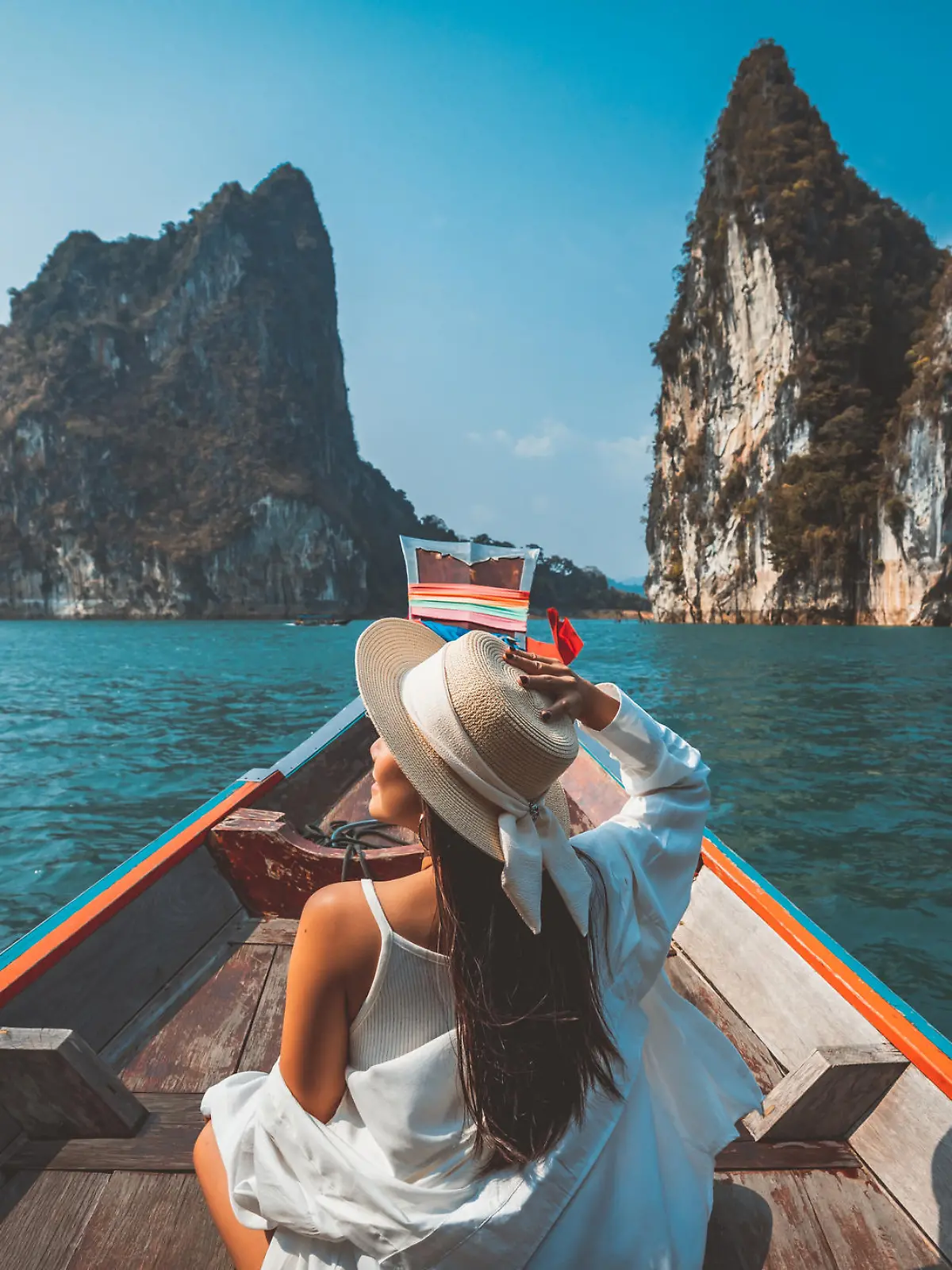 Travel summer vacation concept, Happy solo traveler asian woman with hat relax and sightseeing on Thai longtail boat in Ratchaprapha Dam at Khao Sok National Park, Surat Thani Province, Thailand